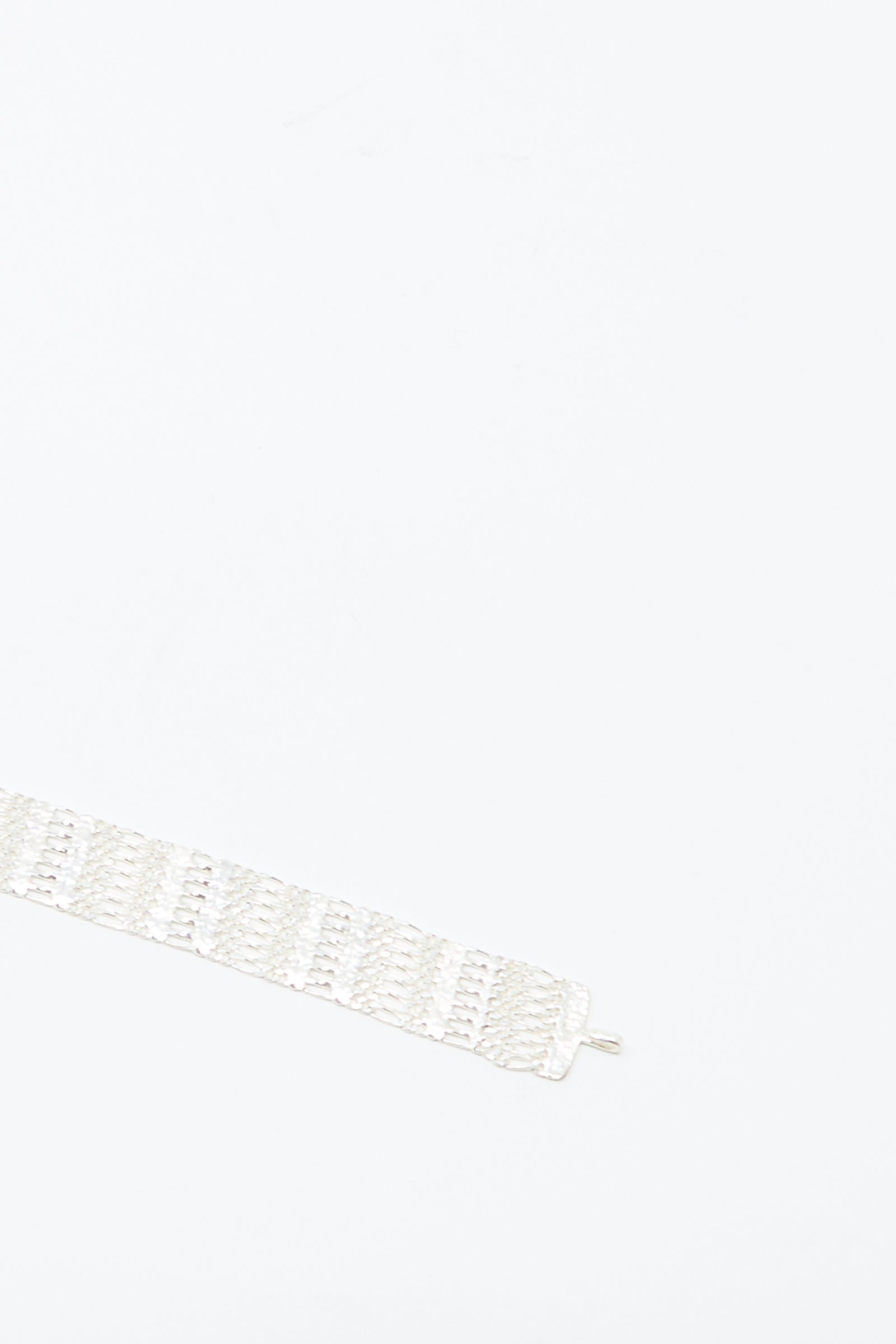 The Friendship Bracelet in Silver by Hannah Keefe, a wide handmade sterling silver chain with a textured pattern, is placed diagonally in the lower left corner on a plain white background.