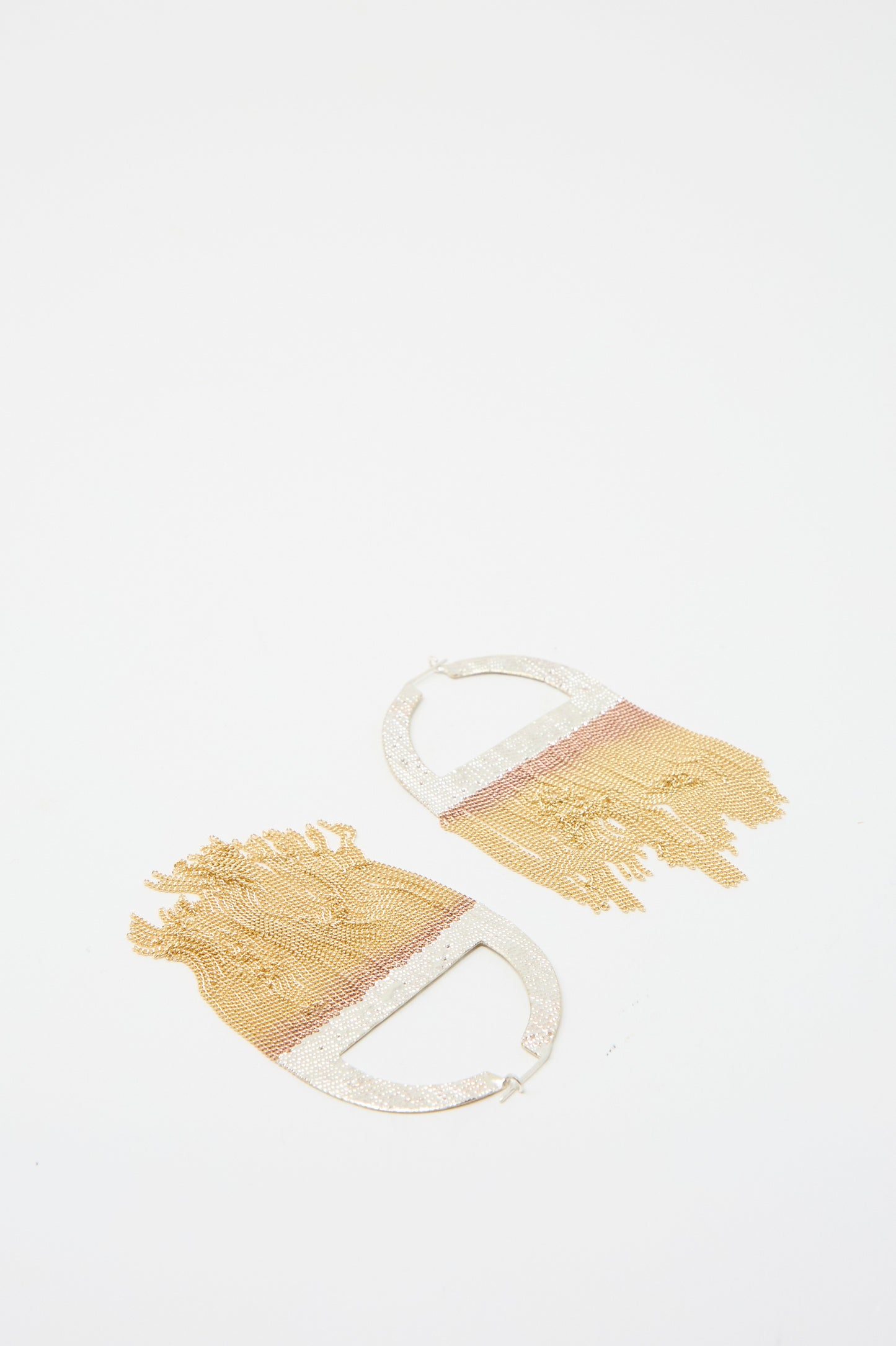 The Sunrise Hoops in Brass and Silver by Hannah Keefe are two earrings featuring soldered silver arches, adorned with brass chain fringe. against a white background.