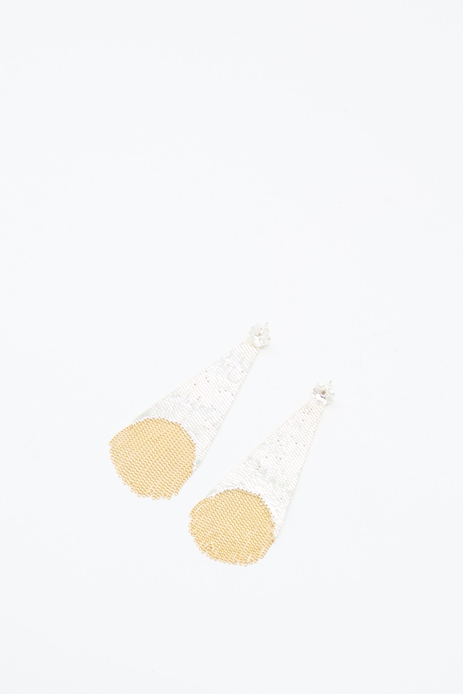 The Teardrop Earrings in Brass and Silver by Hannah Keefe, handmade in California, feature long triangular drops with a silver upper part and circular gold detail at the bottom, shown on a white background.