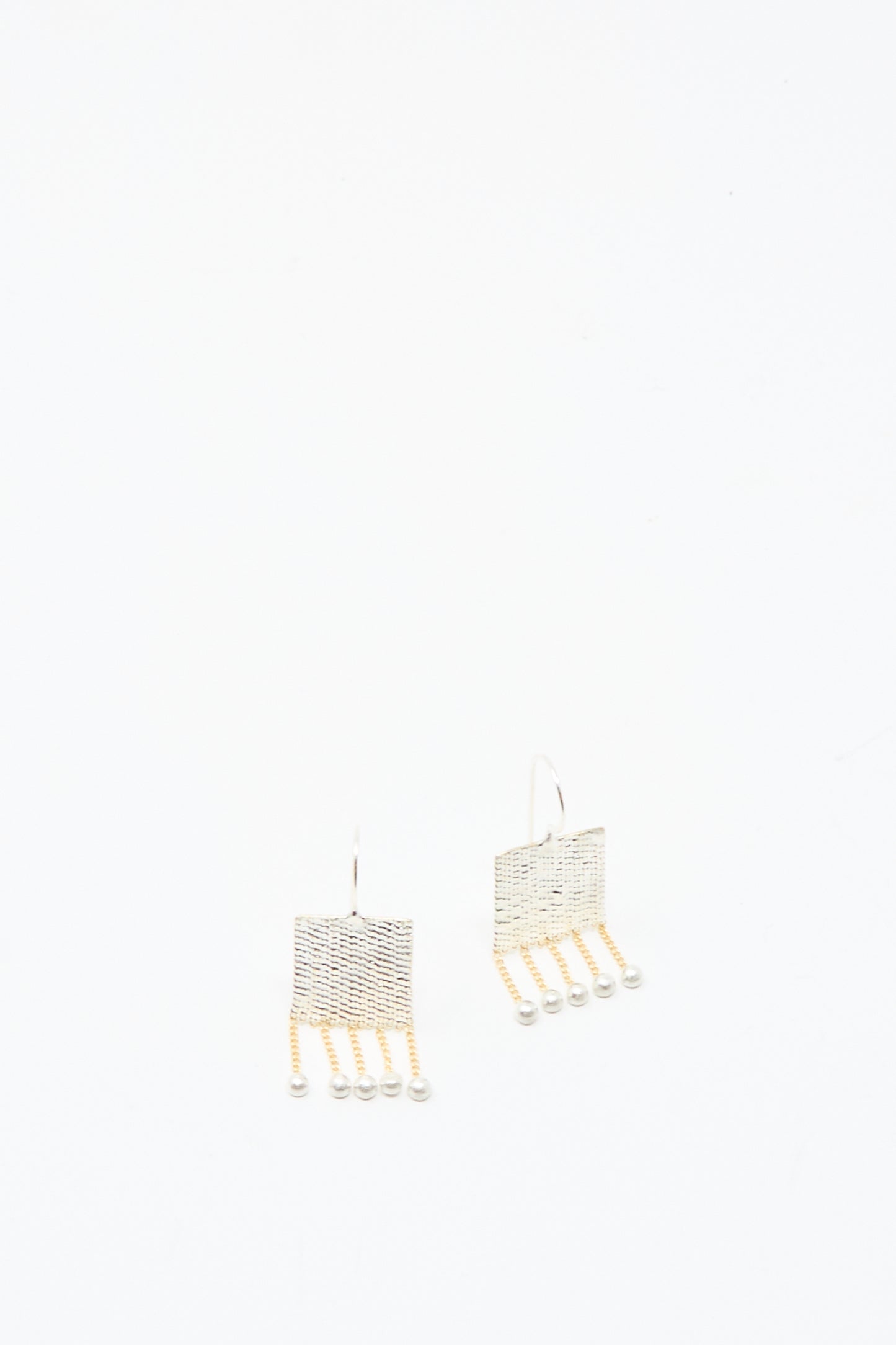 The Bauble Earrings in Brass and Silver by Hannah Keefe feature handmade square shapes with dangling brass chain strands ending in small beads, shown against a plain white background.