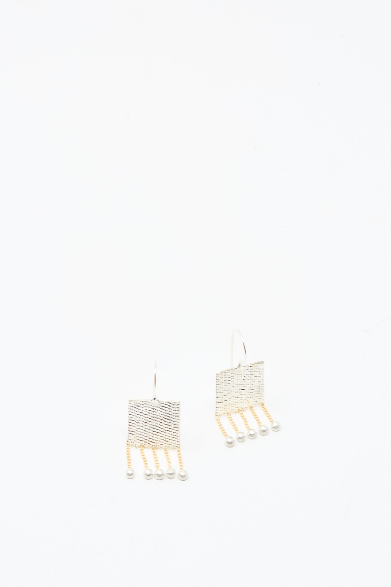 The Bauble Earrings in Brass and Silver by Hannah Keefe feature handmade square shapes with dangling brass chain strands ending in small beads, shown against a plain white background.