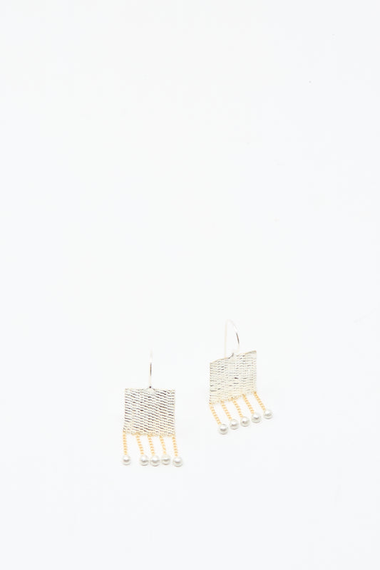 The Bauble Earrings in Brass and Silver by Hannah Keefe feature handmade square shapes with dangling brass chain strands ending in small beads, shown against a plain white background.