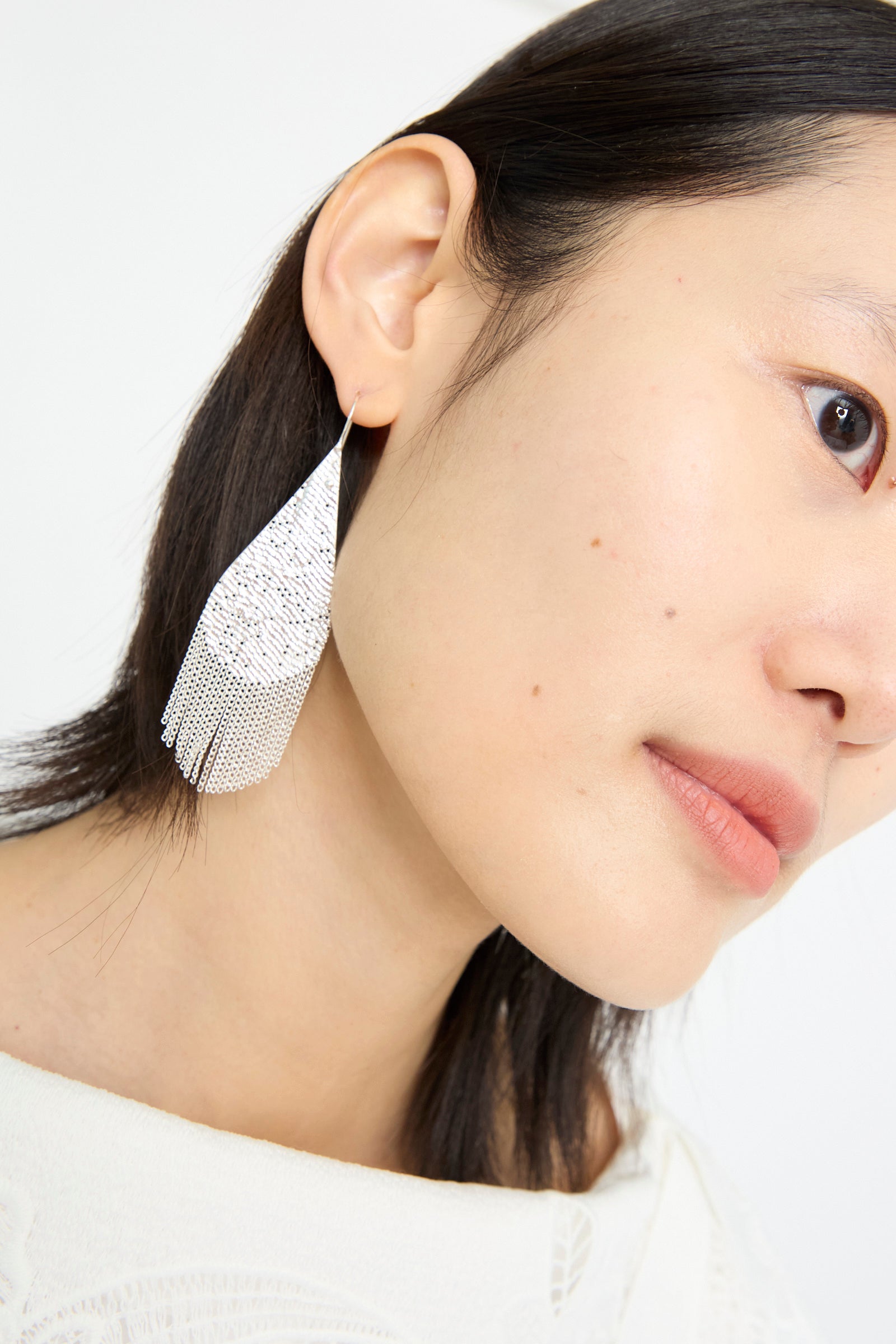 A person displays a Hannah Keefe Drip Earring in Silver against a plain white background, their head tilted slightly.