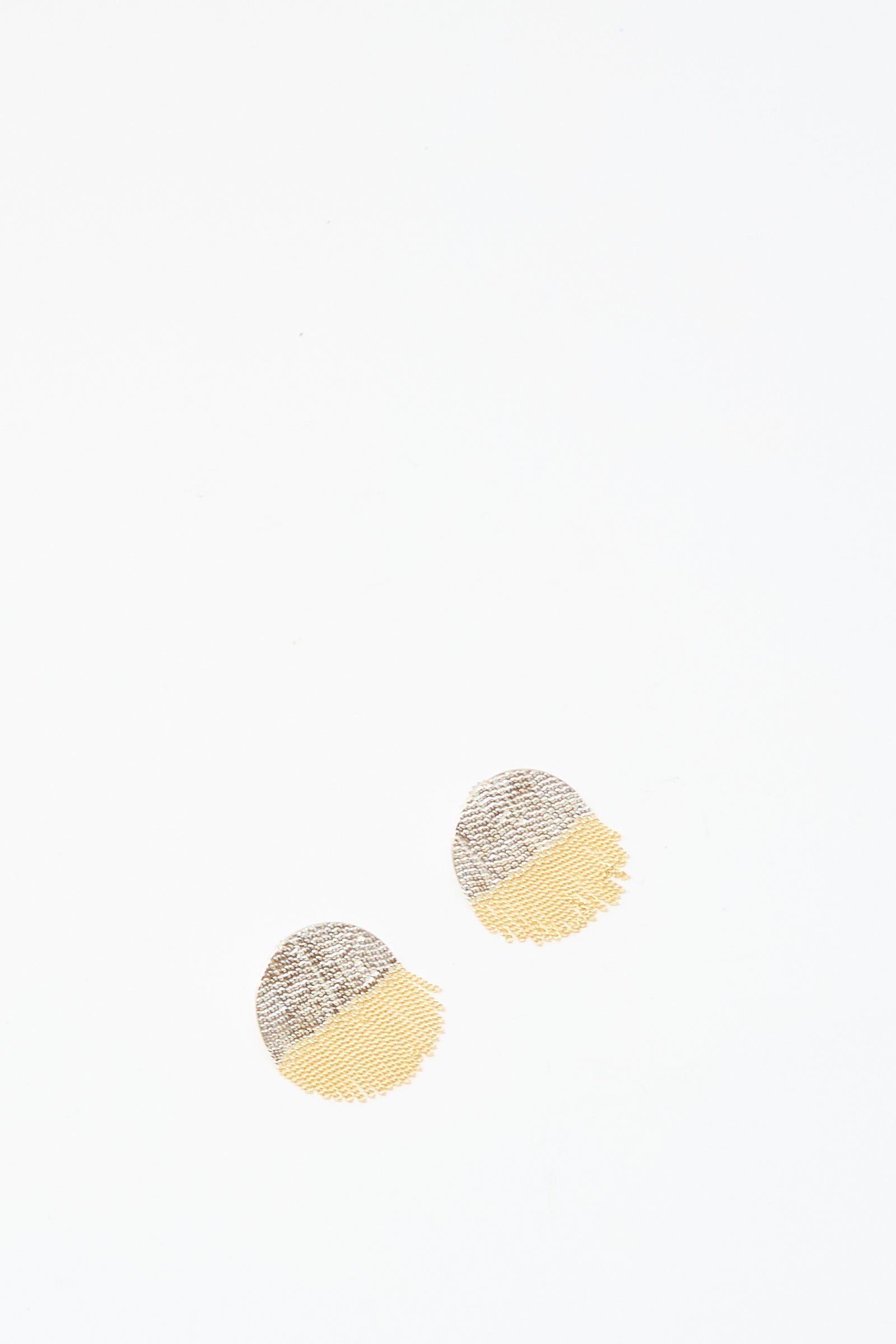 Two Half Circle Studs in Brass and Silver by Hannah Keefe, featuring textured round shapes with gray silver tops and yellow brass bottoms, are placed near the center on a white background.