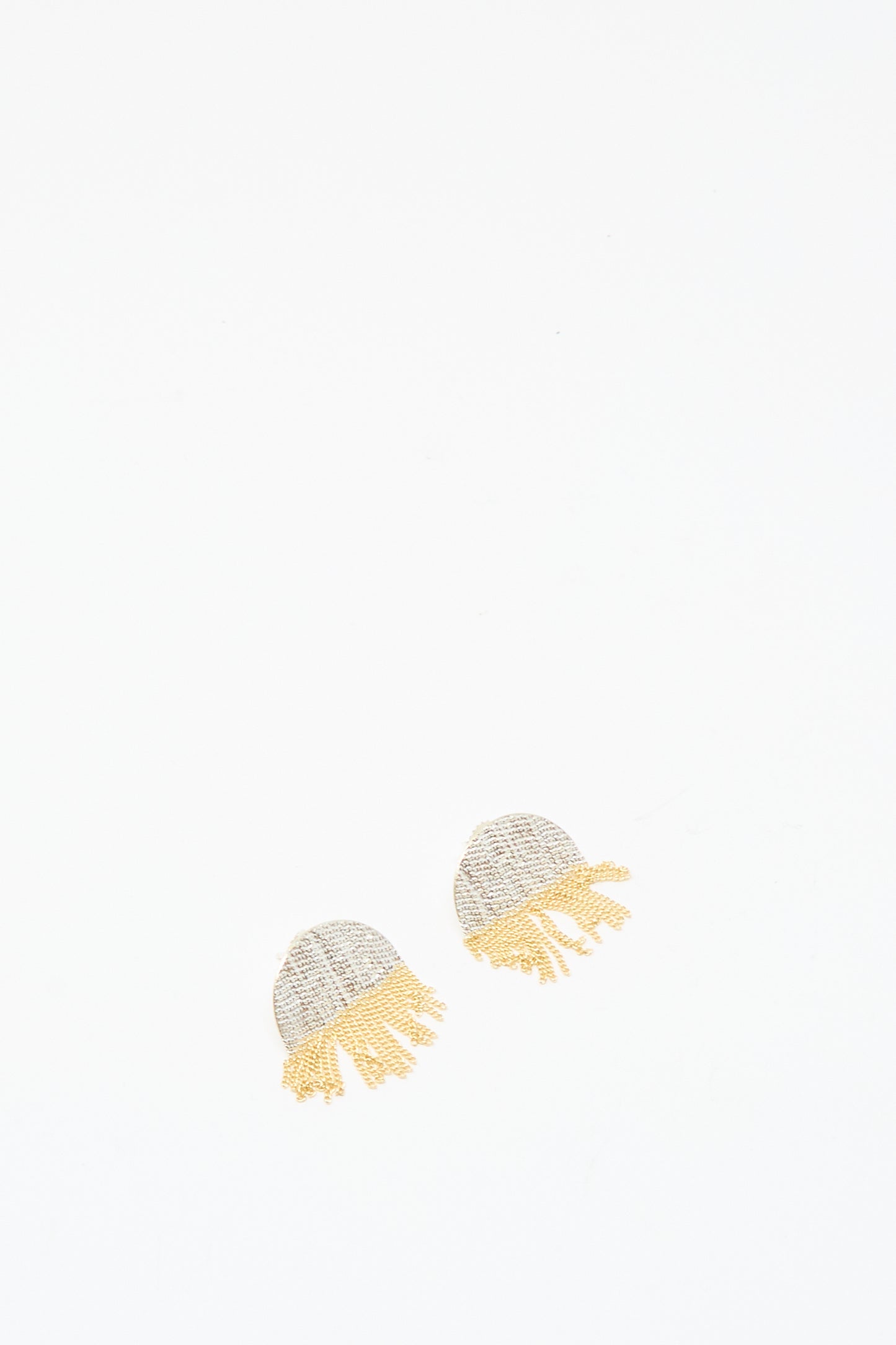 The Half Circle Studs in Brass and Silver by Hannah Keefe, featuring small handmade earrings with light gray tops and yellow brass chain fringe, are displayed on a plain white background.