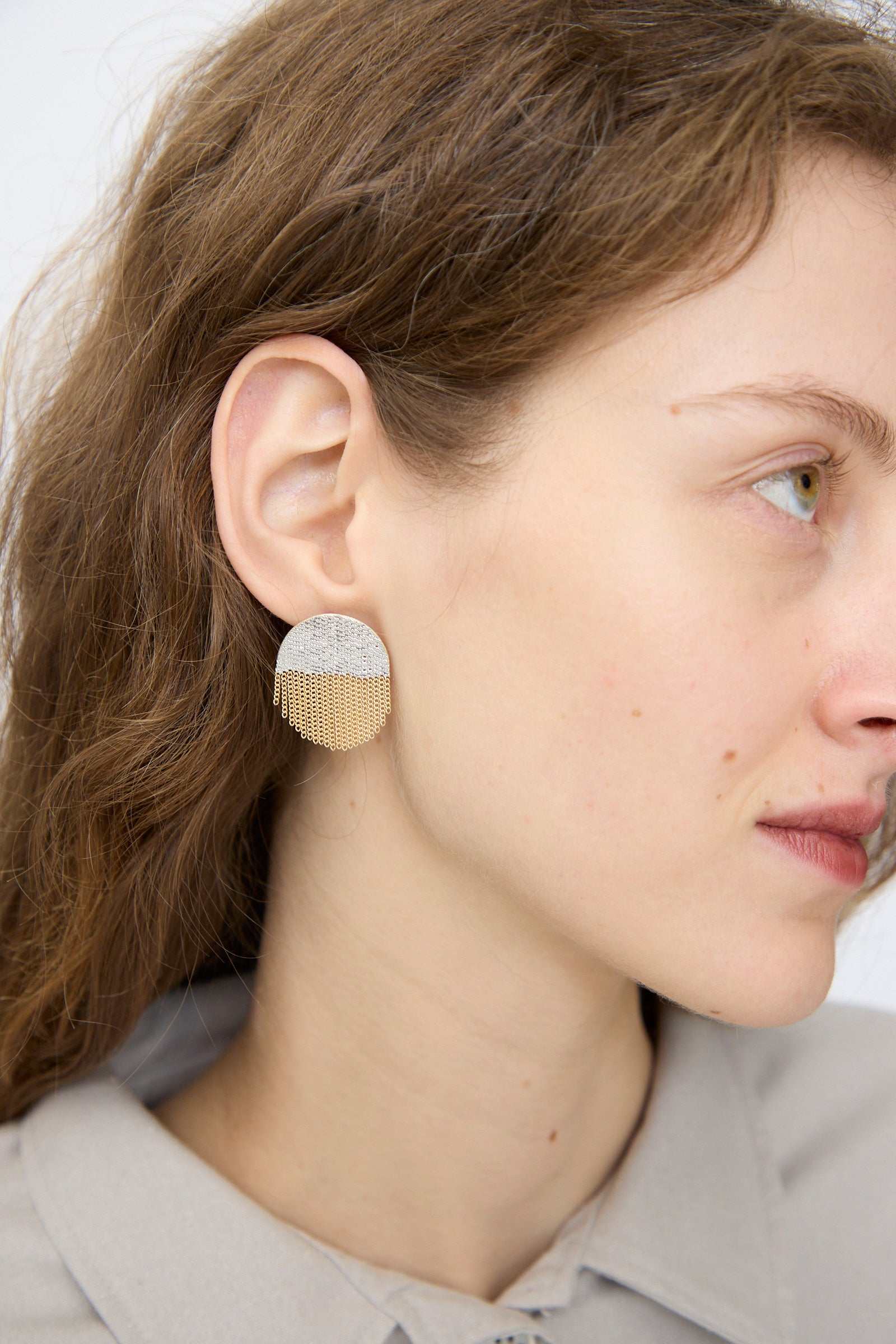 Close-up of a woman wearing Hannah Keefe’s Half Circle Studs in Brass and Silver—handmade in California, featuring silver tops with brass chain fringe—set against a plain background.