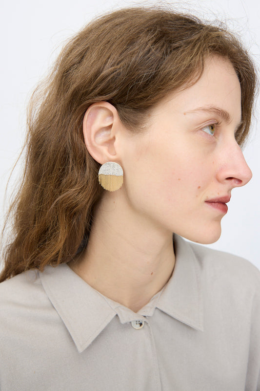 A person with long brown hair, in a beige collared shirt, wears Hannah Keefe's Half Circle Studs in Brass and Silver, shown in profile against a plain light background.