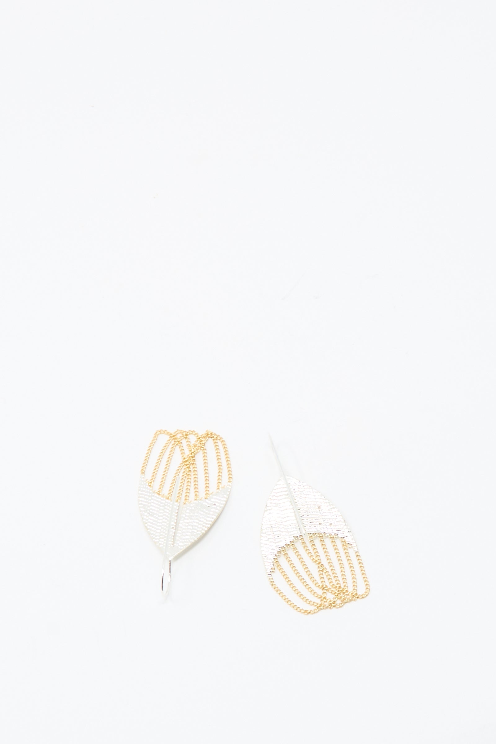 The Scarab Earrings by Hannah Keefe feature handmade leaf-inspired hooks in brass and silver with delicate chain accents, displayed on a plain white background.