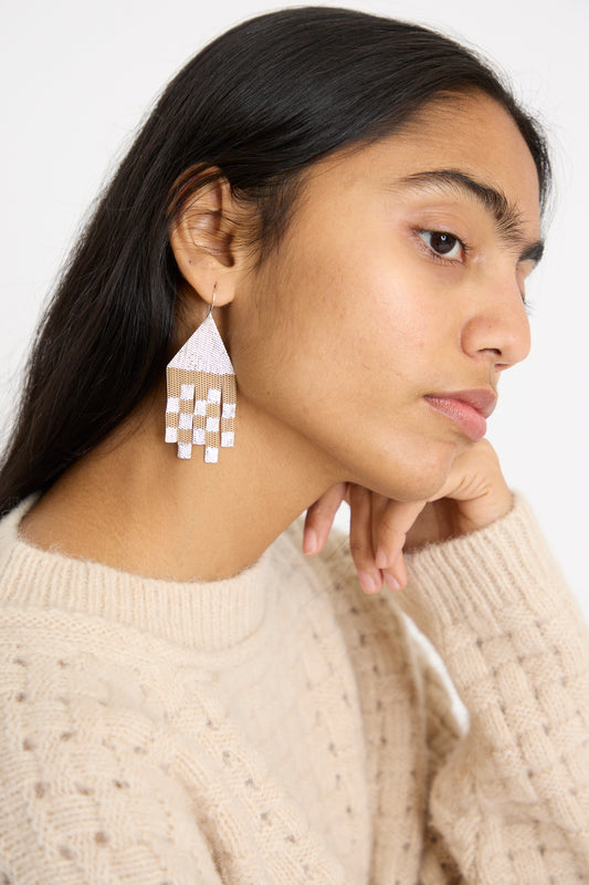 A person wearing a beige sweater and handmade triangle drop earrings gazes thoughtfully to the side against a plain background. The Scotch Earrings by Hannah Keefe, expertly crafted from silver soldered brass in California, add intrigue to their pose.