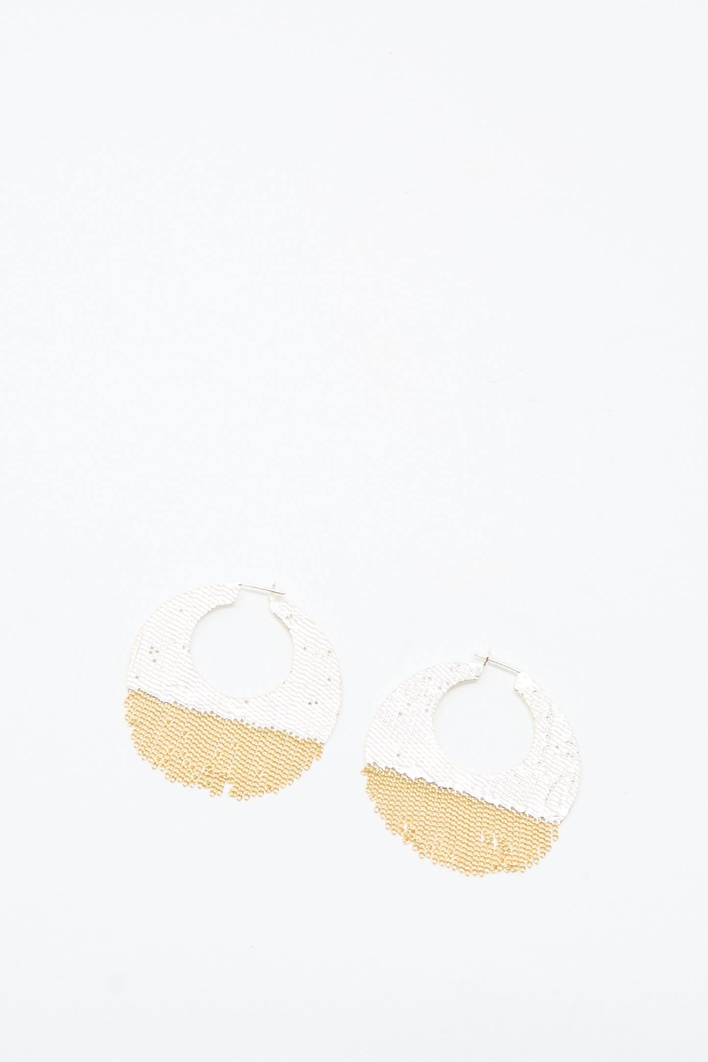 The True Hoops in Brass and Silver by Hannah Keefe are handcrafted round earrings with a textured design, featuring a white upper half and gold lower half. Displayed on a plain white background.