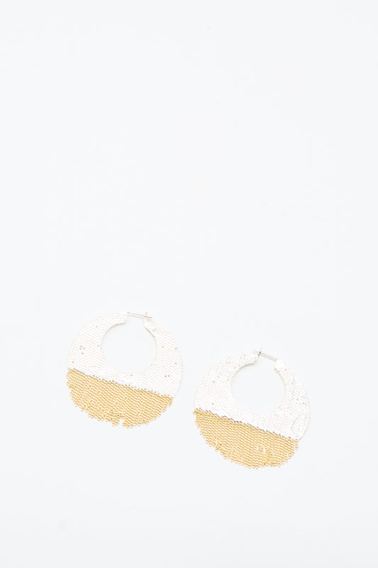 The True Hoops in Brass and Silver by Hannah Keefe are handcrafted round earrings with a textured design, featuring a white upper half and gold lower half. Displayed on a plain white background.