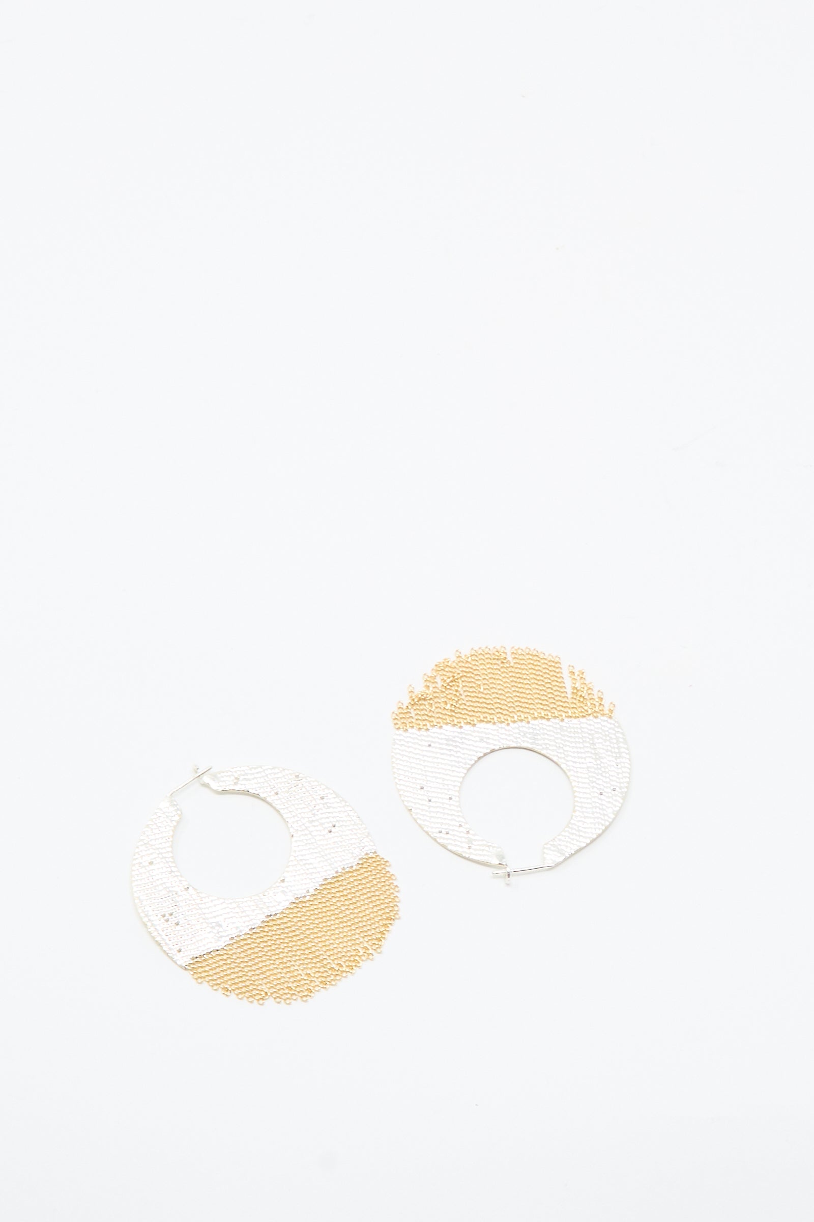The True Hoops in Brass and Silver by Hannah Keefe are circular earrings featuring white and gold beaded sections, displayed on a plain white background.