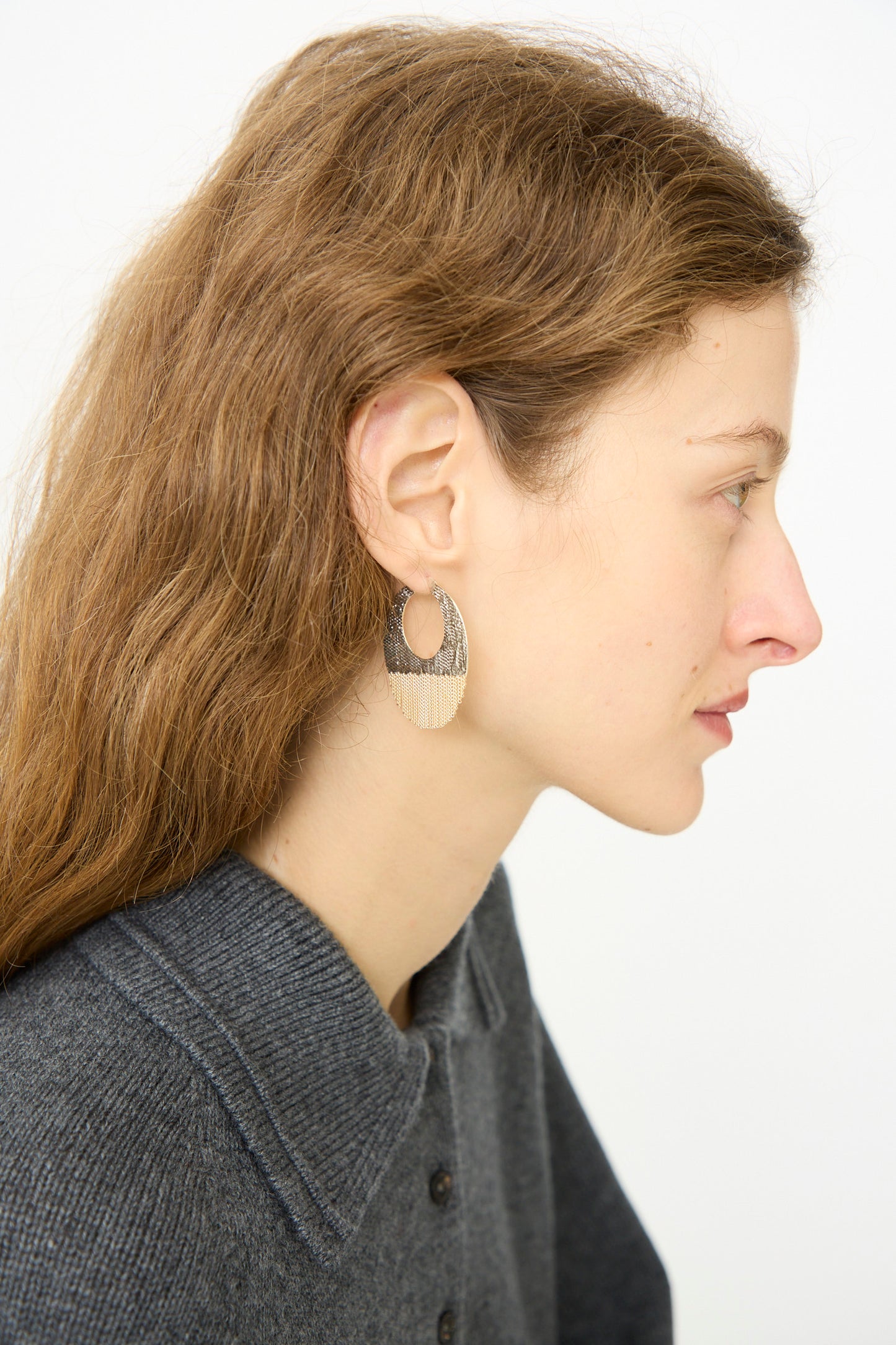Woman with long brown hair wears the Hannah Keefe True Hoops in Brass and Silver, shown in profile against a plain white background, paired with a gray collared sweater.