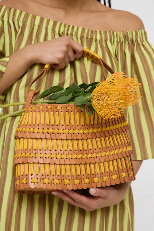 Woman holding a Hatori Basket Bag 168 in Tan and Yellow with a pincushion protea inside.