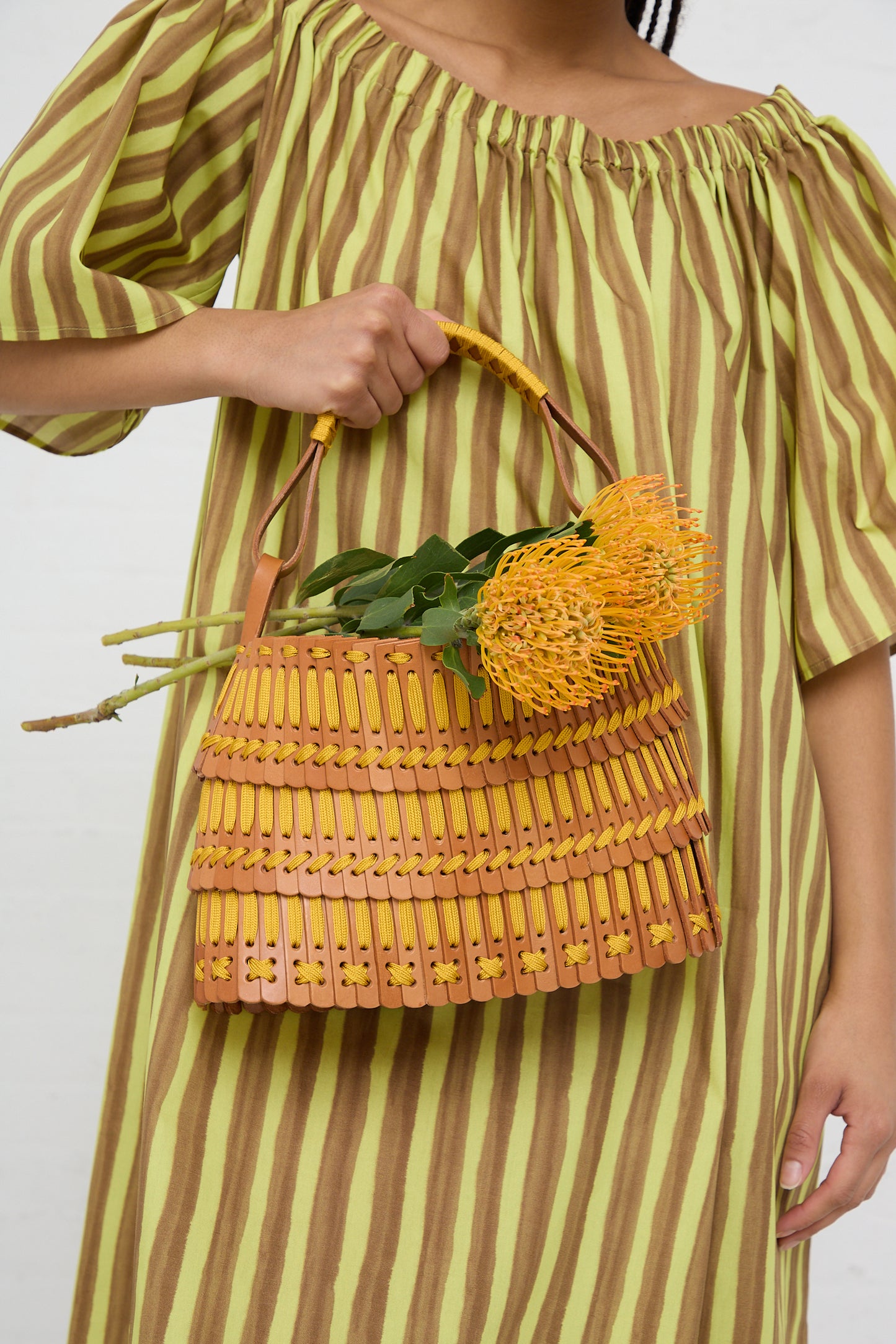 Woman holding a Hatori Basket Bag 168 in Tan and Yellow with yellow flowers against a striped dress background.