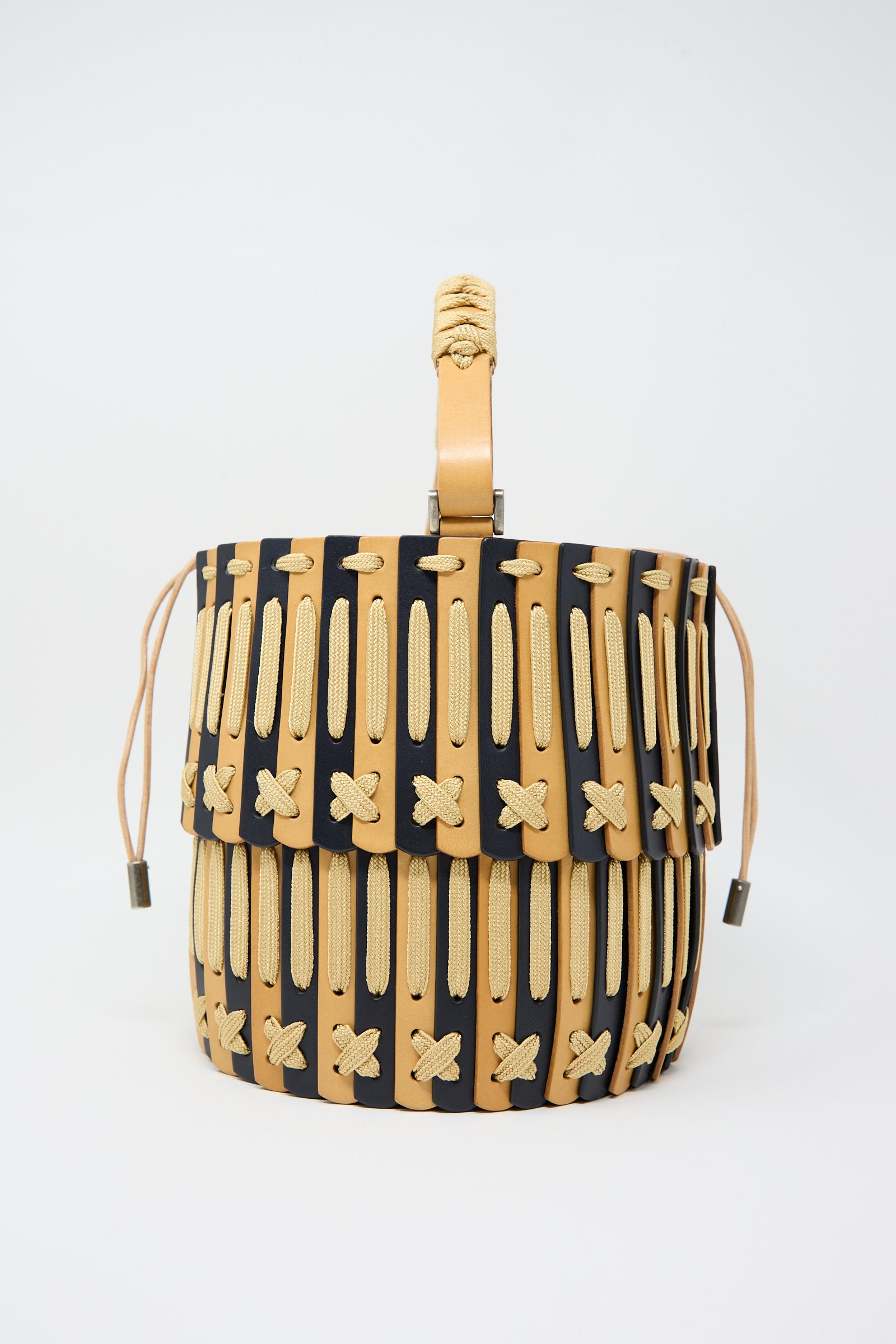 Hatori's Leather Bucket Bag in Natural and Midnight Blue features a tan and black woven vegetable-tanned leather design, a braided handle, beige cross-stitch detailing, and an adjustable strap.