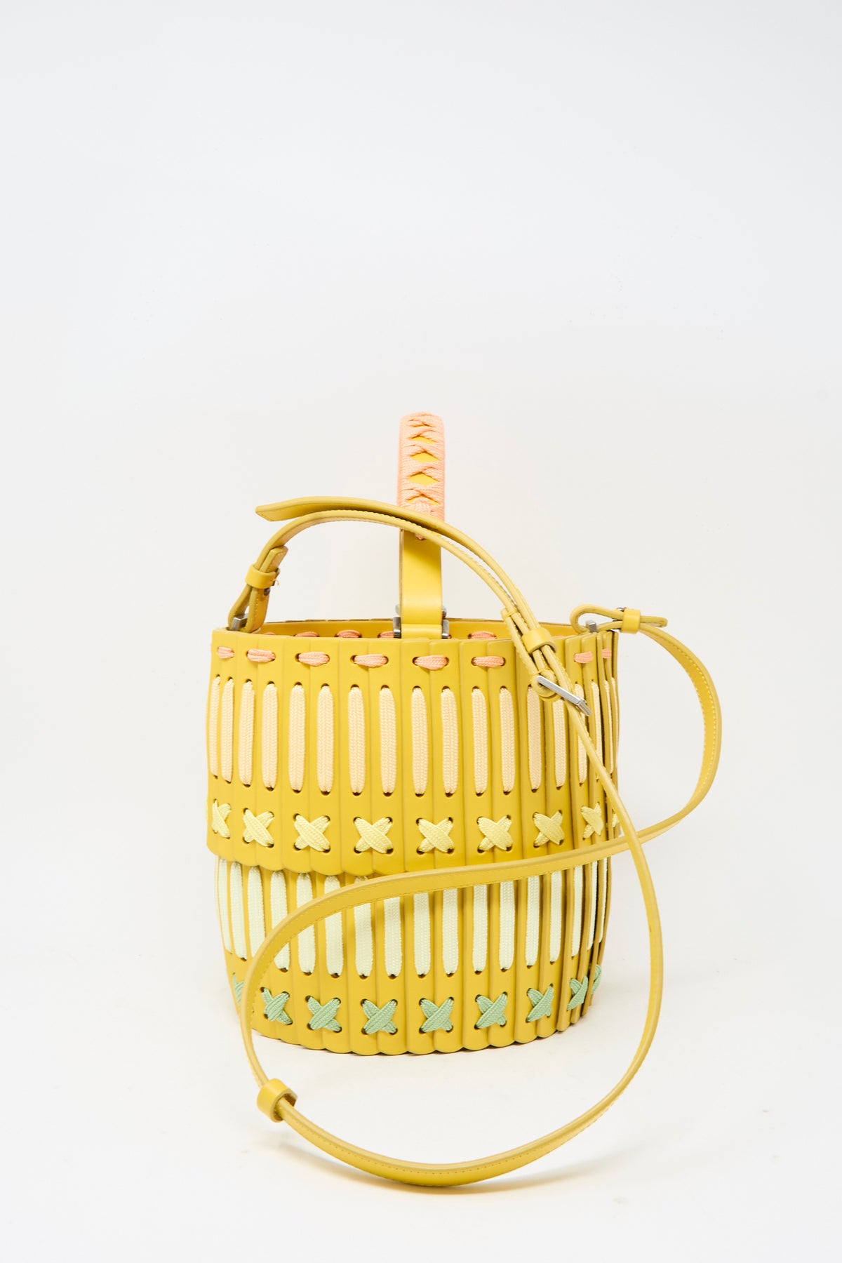 Handcrafted in Japan, the Hatori Leather Bucket 80 Artist Edition with Holly Coulis in Yellow is a bucket-style handbag with vertical slots, pastel crisscross lacing, a top handle, and shoulder strap.