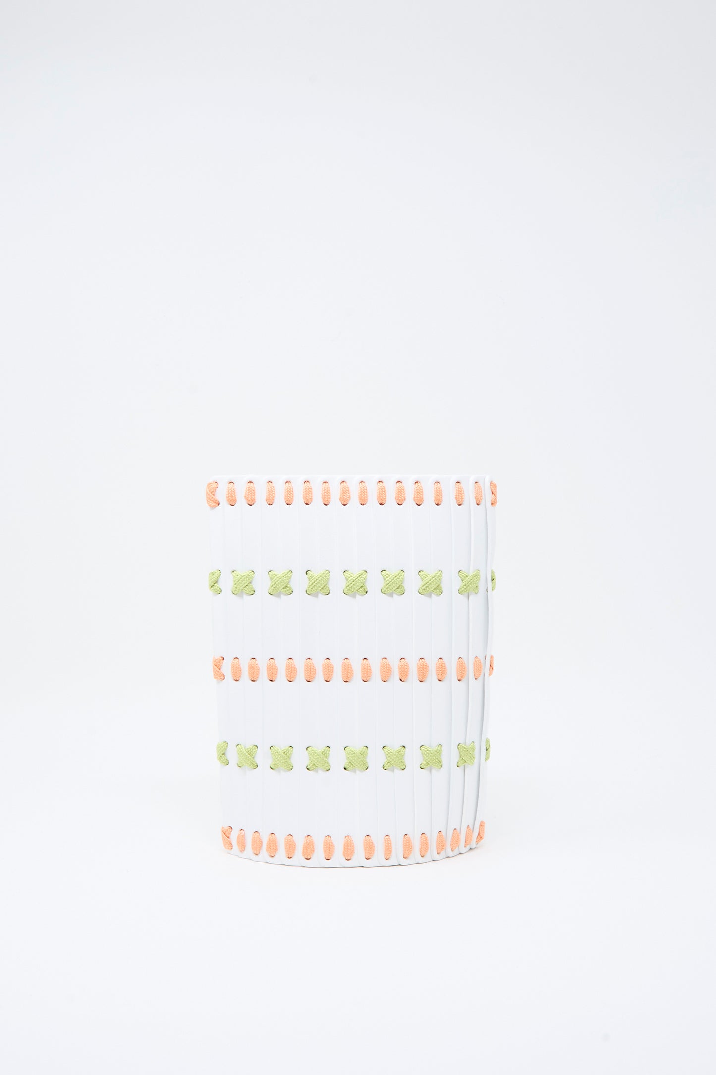 A white crossbody bag from Hatori, named the Leather Crossbody 30, featuring intricate multi-colored lacing in orange and green forming X-shaped patterns across its surface, reminiscent of handcrafted designs, set against a plain white background.