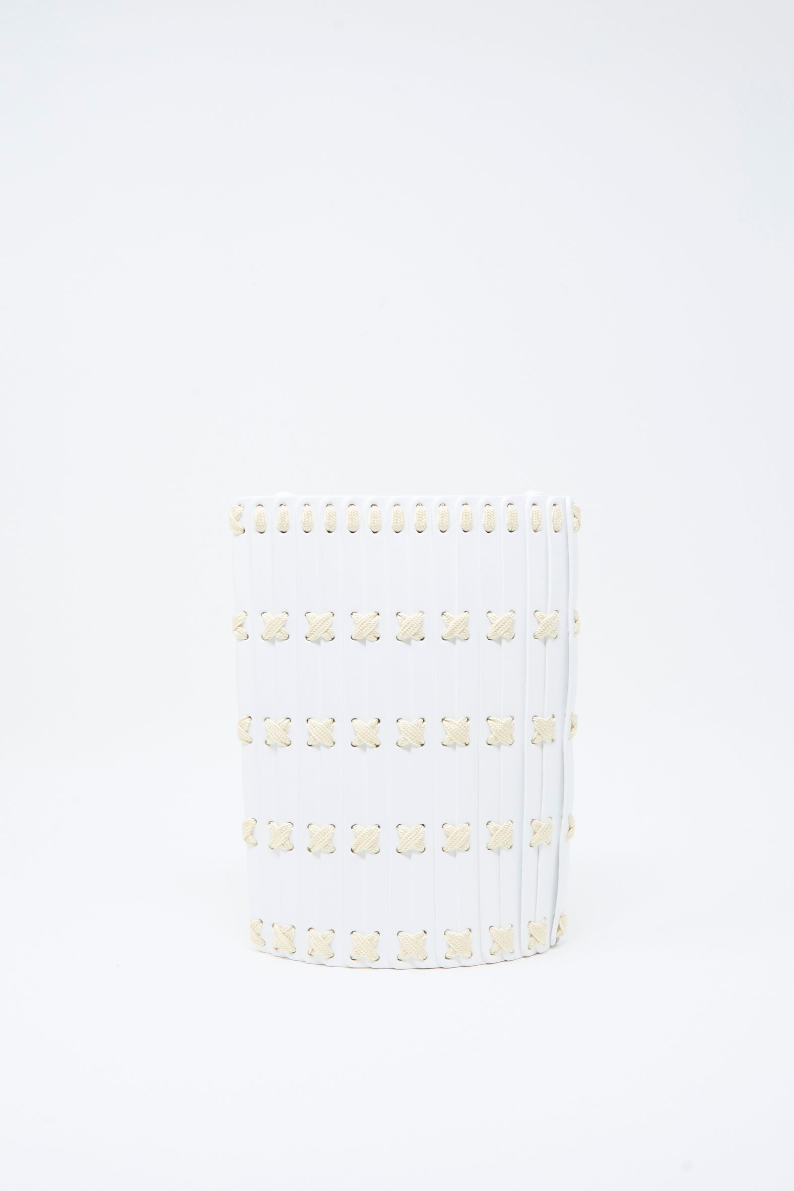 A white cylindrical Leather Crossbody 30 by Hatori, featuring vertical ridges and a grid of small, beige floral motifs reminiscent of the delicate patterns found on handcrafted vegetable-tanned leather goods, accented with white lacing.