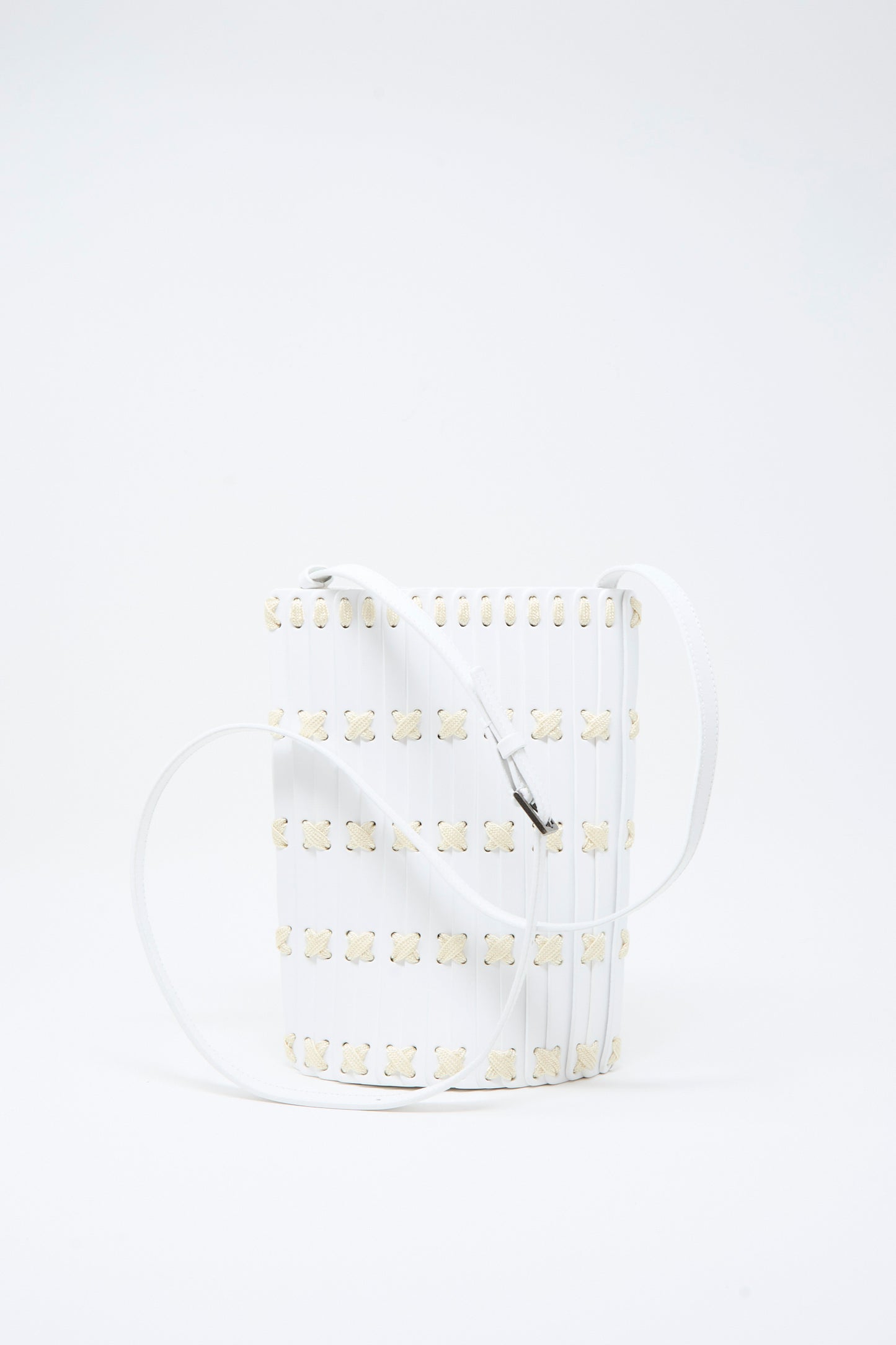 The Hatori Leather Crossbody 30 in White with White Lacing is a handcrafted white bucket bag made from vegetable-tanned leather, featuring a grid pattern of small beige flower-like shapes and a long white strap. It is displayed against a plain white background.
