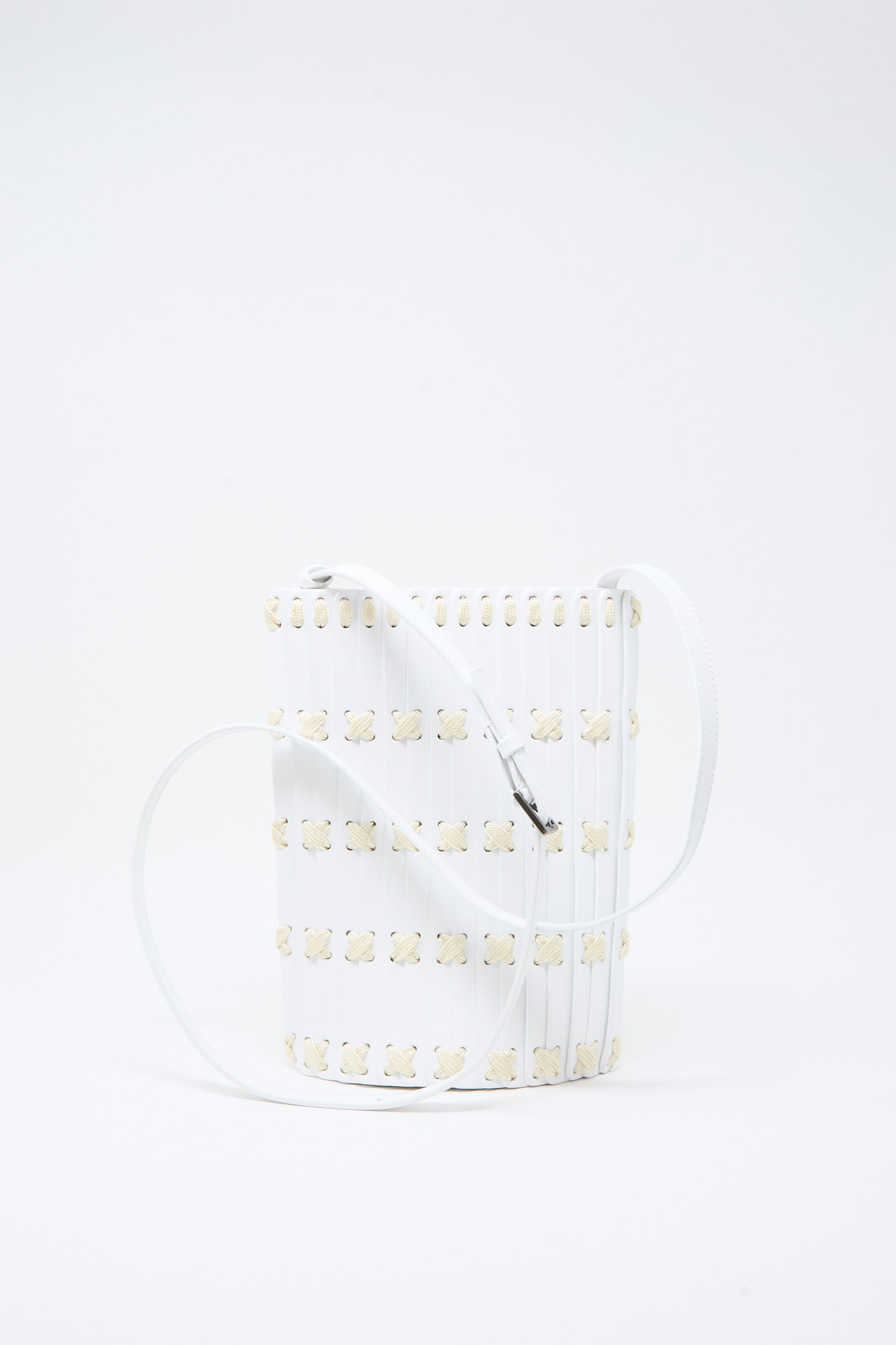 The Hatori Leather Crossbody 30 in White with White Lacing is a handcrafted white bucket bag made from vegetable-tanned leather, featuring a grid pattern of small beige flower-like shapes and a long white strap. It is displayed against a plain white background.