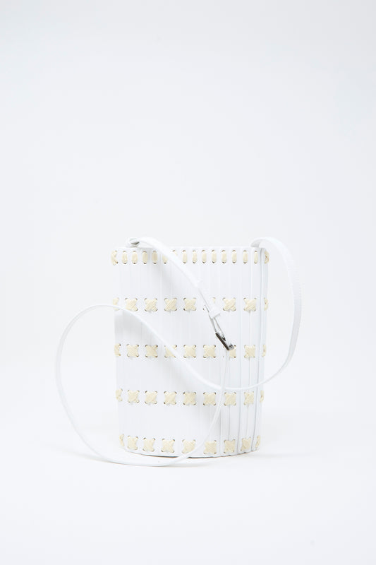 The Hatori Leather Crossbody 30 in White with White Lacing is a handcrafted white bucket bag made from vegetable-tanned leather, featuring a grid pattern of small beige flower-like shapes and a long white strap. It is displayed against a plain white background.