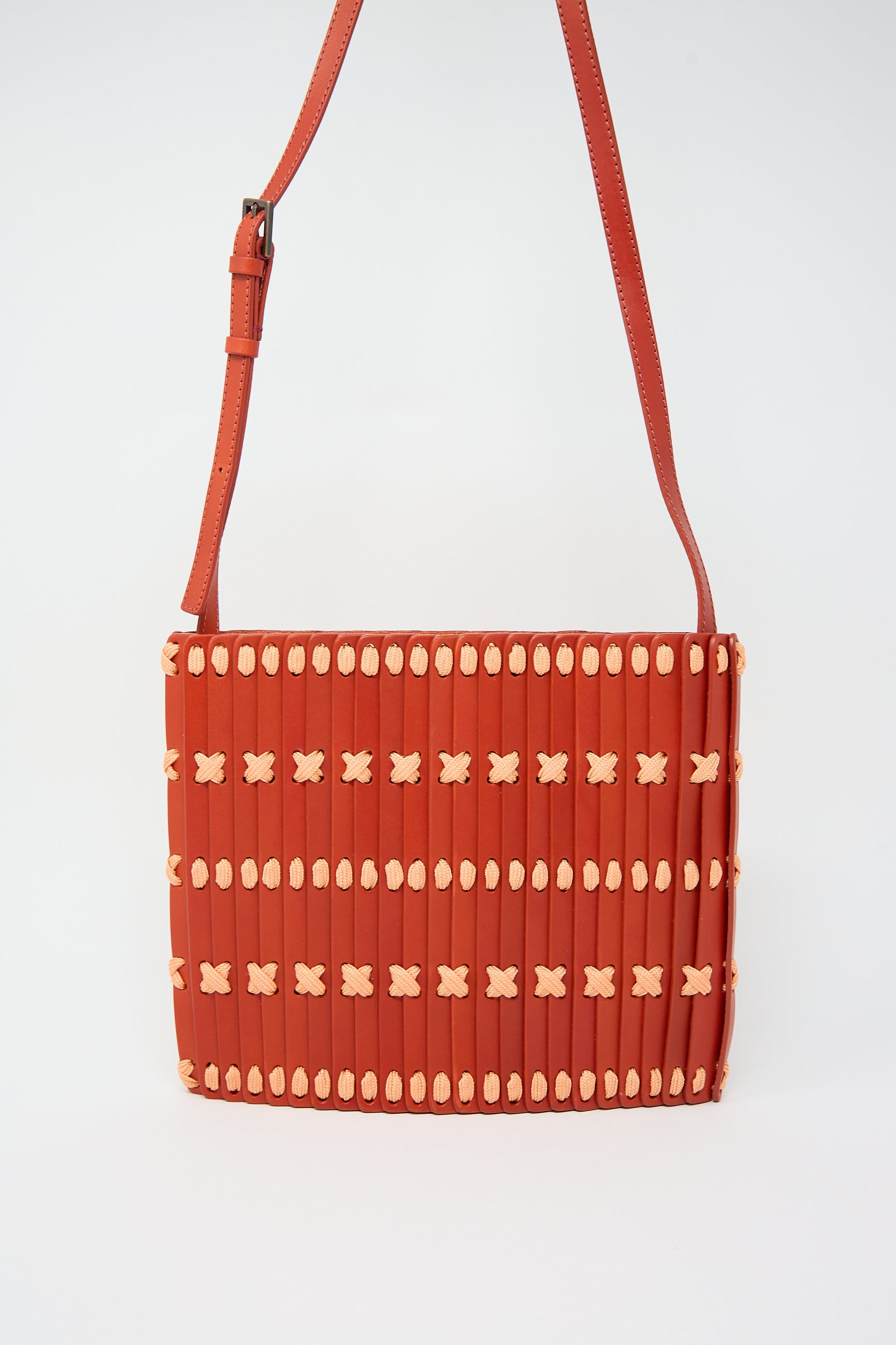 A Hatori Leather Crossbody in Red with Light Coral Lace, featuring an adjustable shoulder strap and a woven pattern with beige accents.