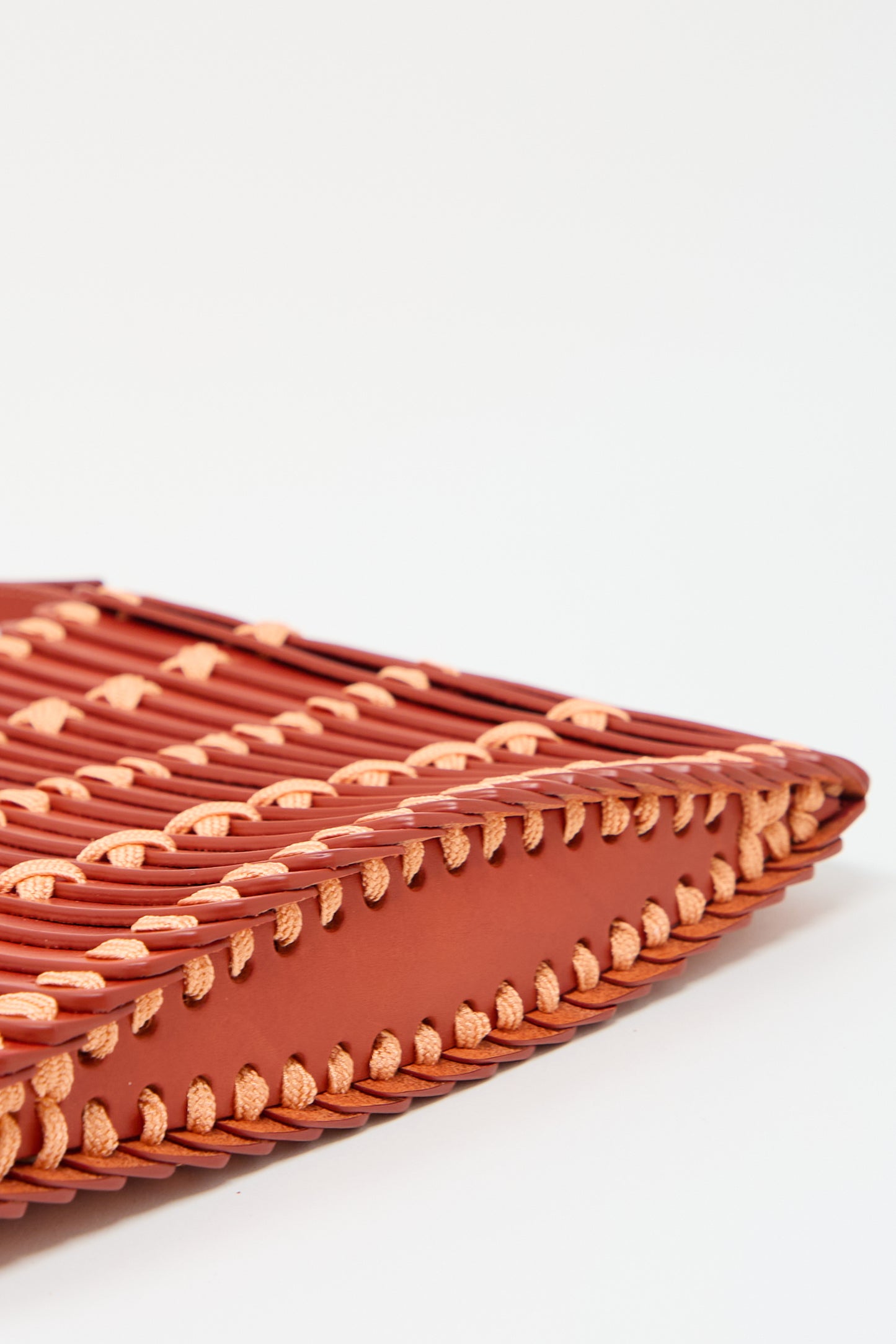 Close-up of the Hatori Leather Crossbody in Red with Light Coral Lace featuring intertwined reddish-brown and light beige strips, showcasing intricate stitching along the edges and an adjustable shoulder strap.