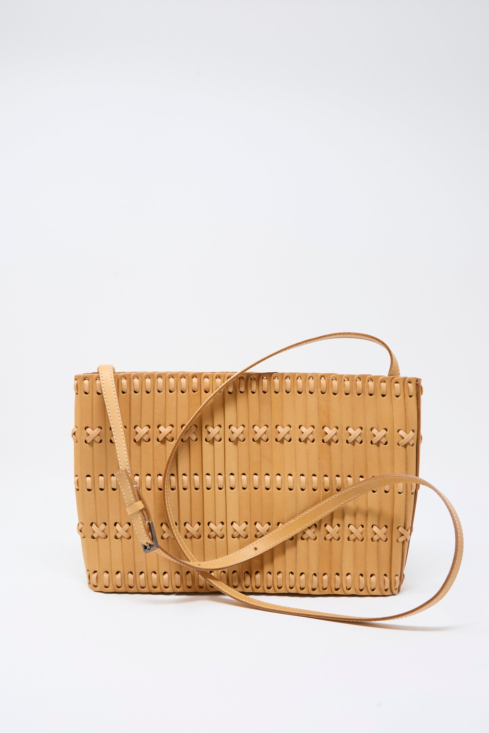 The Hatori Leather Shoulder 60 Bag in Natural with Tan Lacing is a handcrafted crossbody, made from premium vegetable-tanned leather and featuring a long strap. Designed with vertical slits and small X-shaped laced details, this unique shoulder bag is showcased against a plain white background.