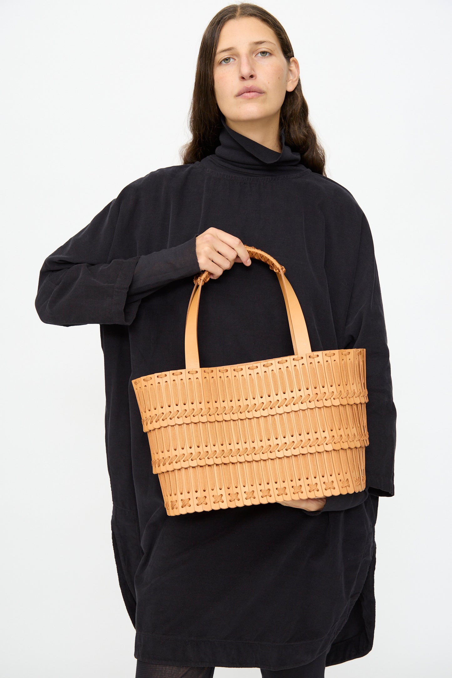 A person in a loose black dress holds the Hatori Leather Tote 198 in Natural with Natural Lace, featuring two handles, against a plain light background.