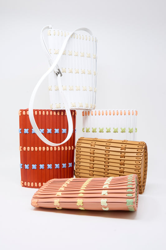 Five Hatori Leather Crossbody 30 Artist Edition handbags, designed in collaboration with Alex Dodge in red, featuring slotted patterns and colored accents crafted from vegetable tanned leather, are arranged together against a plain white background.