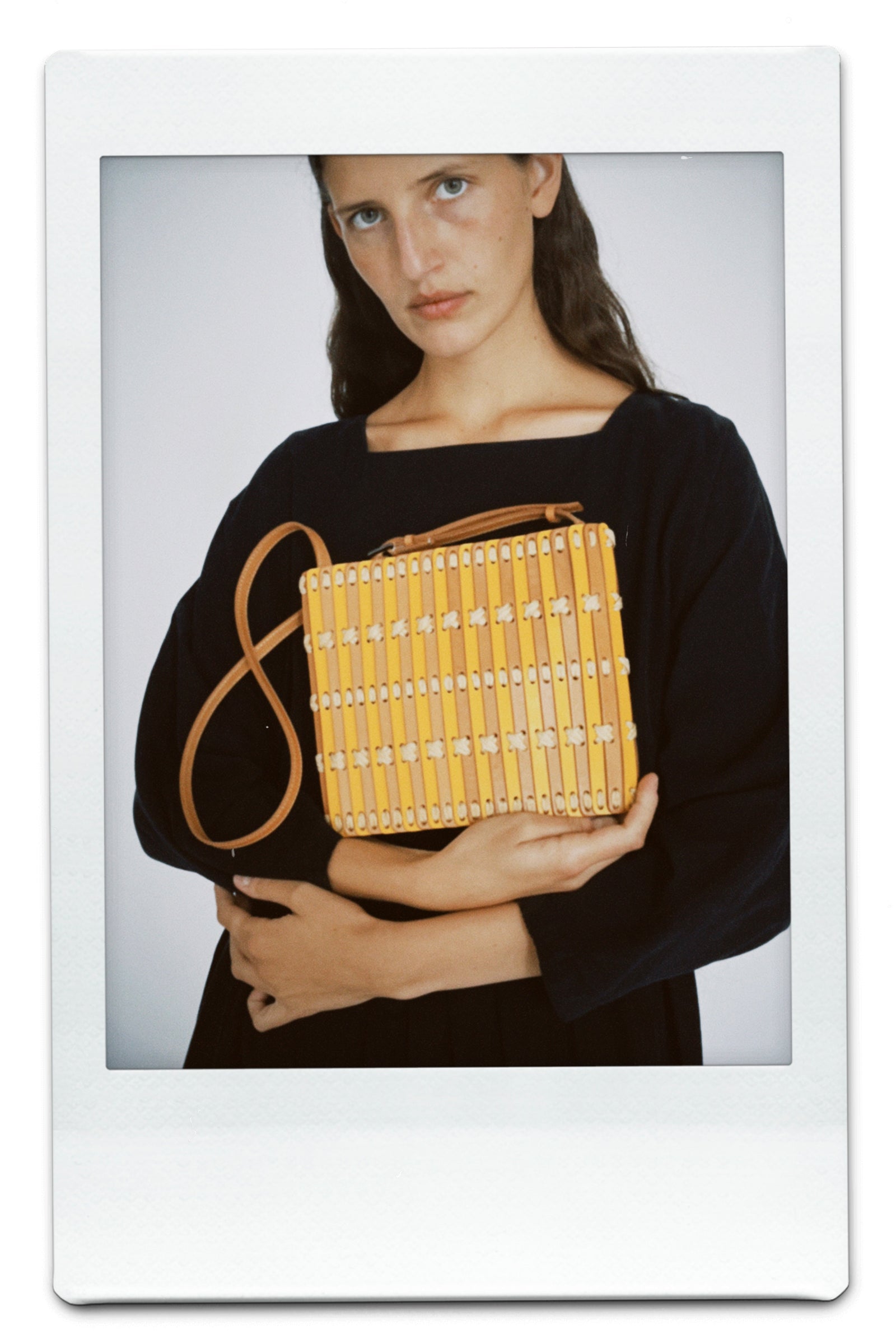 Woman holding a yellow woven handbag against a plain background