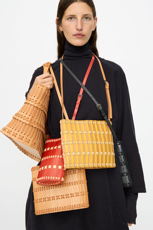 A person in a black long-sleeve dress displays Hatori’s Leather Phone 26 Bag in Tomato with Lemon and Pink Lace, crafted with vegetable tanned leather and refined details made in Tokyo.