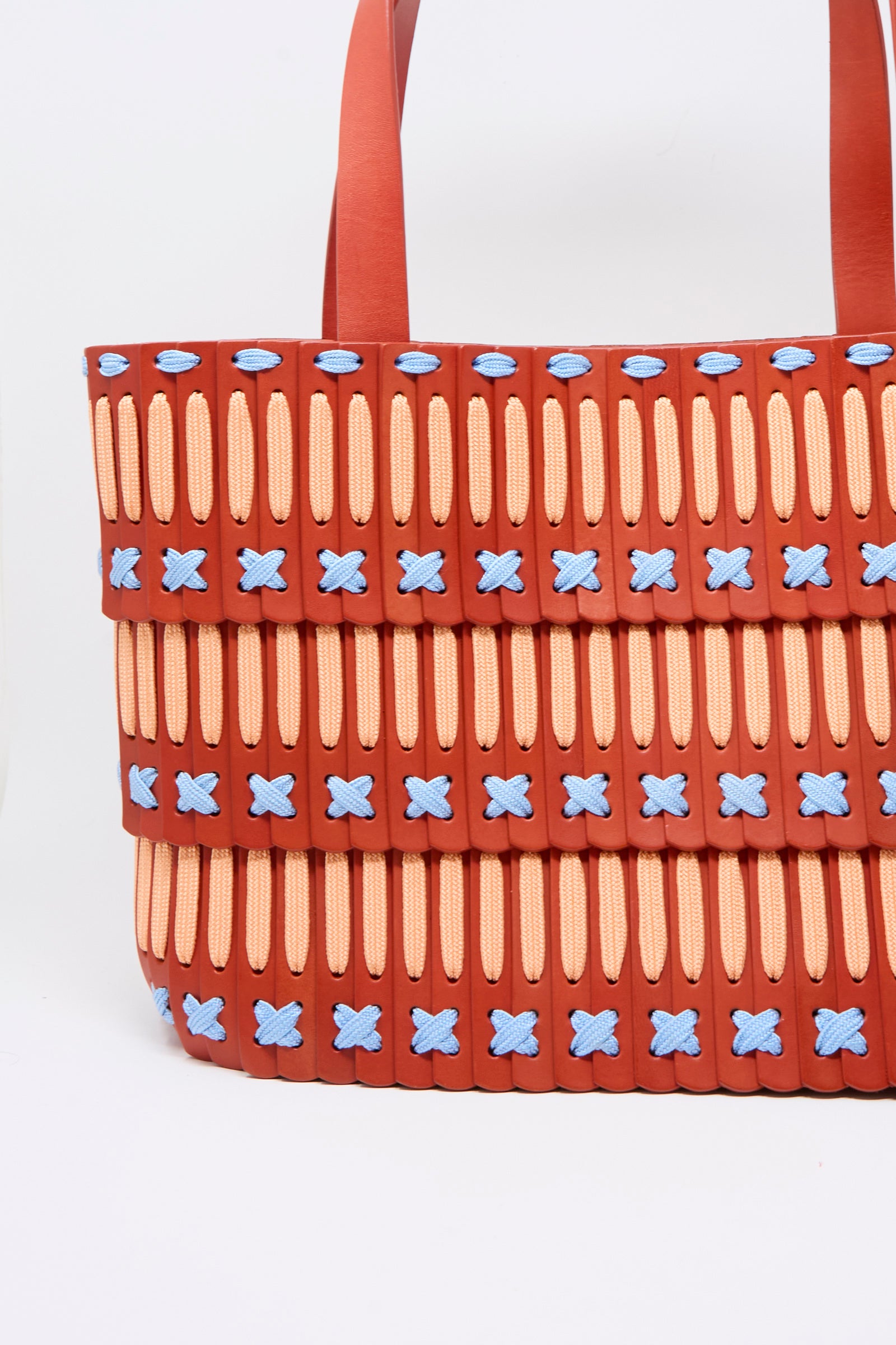 The Hatori Leather Tote 198 Artist Edition with Alex Dodge in Red is a large tote bag, expertly crafted from vegetable tanned leather, featuring a red base, yellow vertical slits, blue X-shaped stitches, layered horizontal panels, and a red strap—all set against a white background.