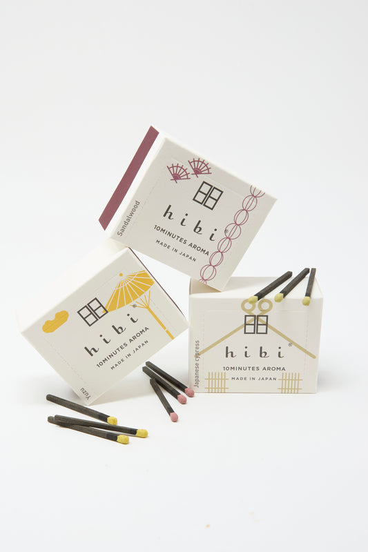 Three boxes of Hibi Incense Matches, featuring minimalist design, are displayed with several handcrafted matches in front.