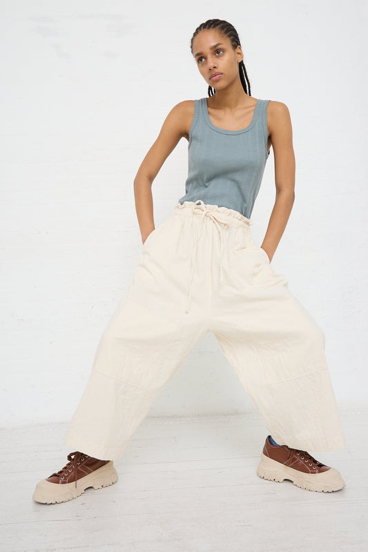 A woman in a blue tank top and Azumadaki Cotton Quilt Pant in Ivory by Ichi Antiquités standing with hands on hips against a white background.