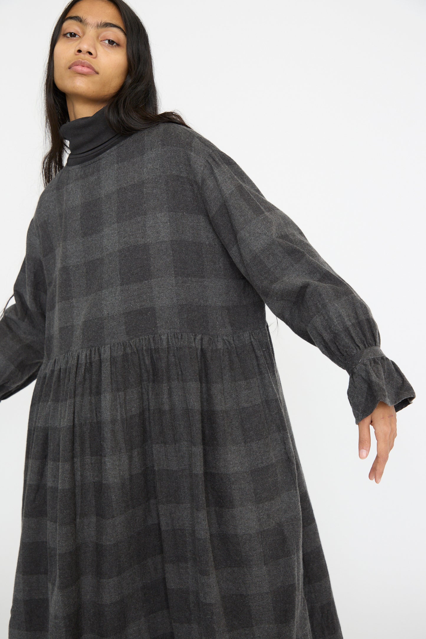 A model wearing the Ichi Antiquités Block Check Flannel Dress in Charcoal with long sleeves, ruffled cuffs, and a relaxed fit.