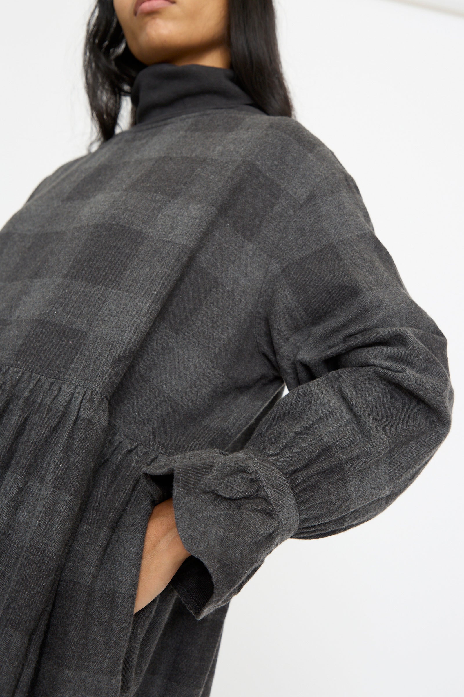 A person stands against a white backdrop wearing the Block Check Flannel Dress in Charcoal by Ichi Antiquités, seen below the chin. 