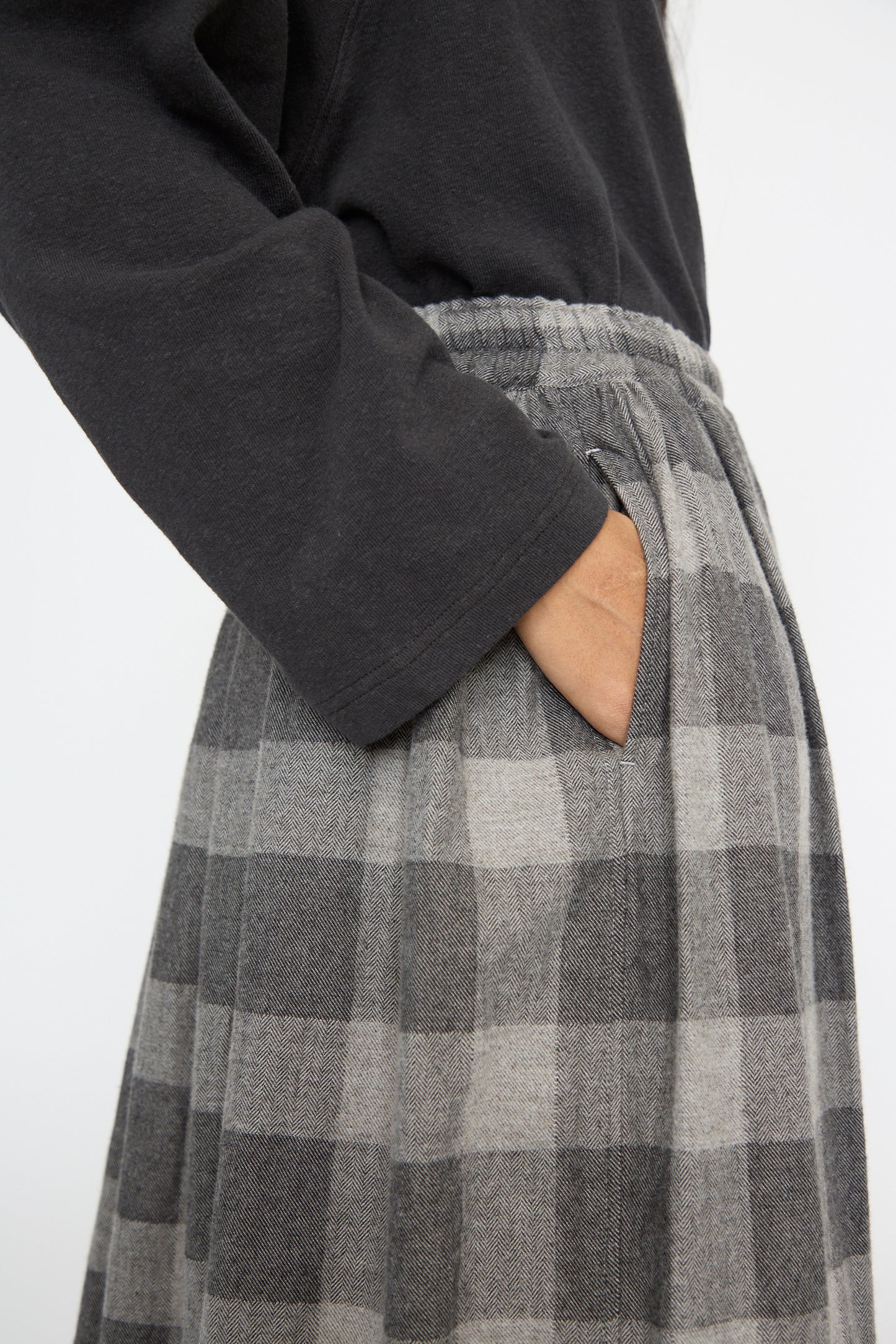 A person wearing a dark long-sleeve shirt and the Ichi Antiquités Block Check Flannel Skirt in Gray, with one hand in the pocket, showcasing an elegant A-line silhouette.