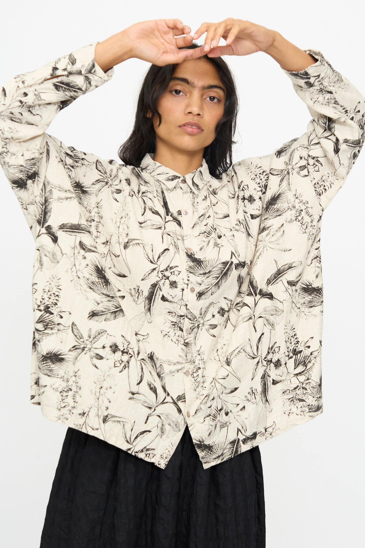 A person wearing the Ichi Antiquités Botanical Print Shirt in Natural with a black skirt, arms raised above their head, poses against a plain white background.