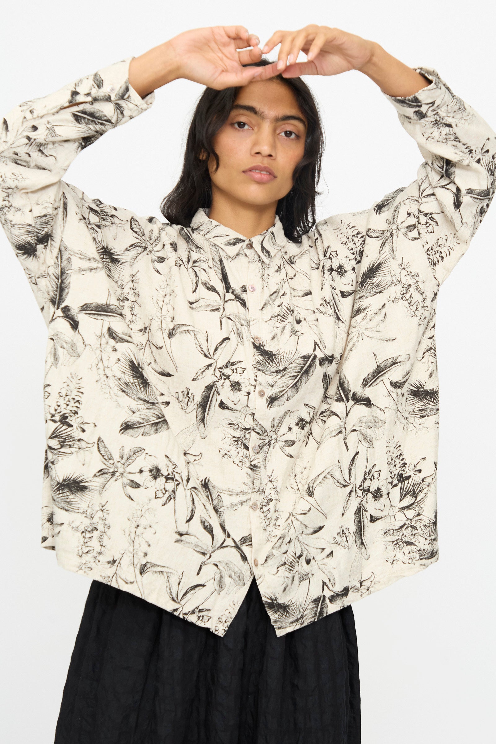 A person wearing the Ichi Antiquités Botanical Print Shirt in Natural with a black skirt, arms raised above their head, poses against a plain white background.