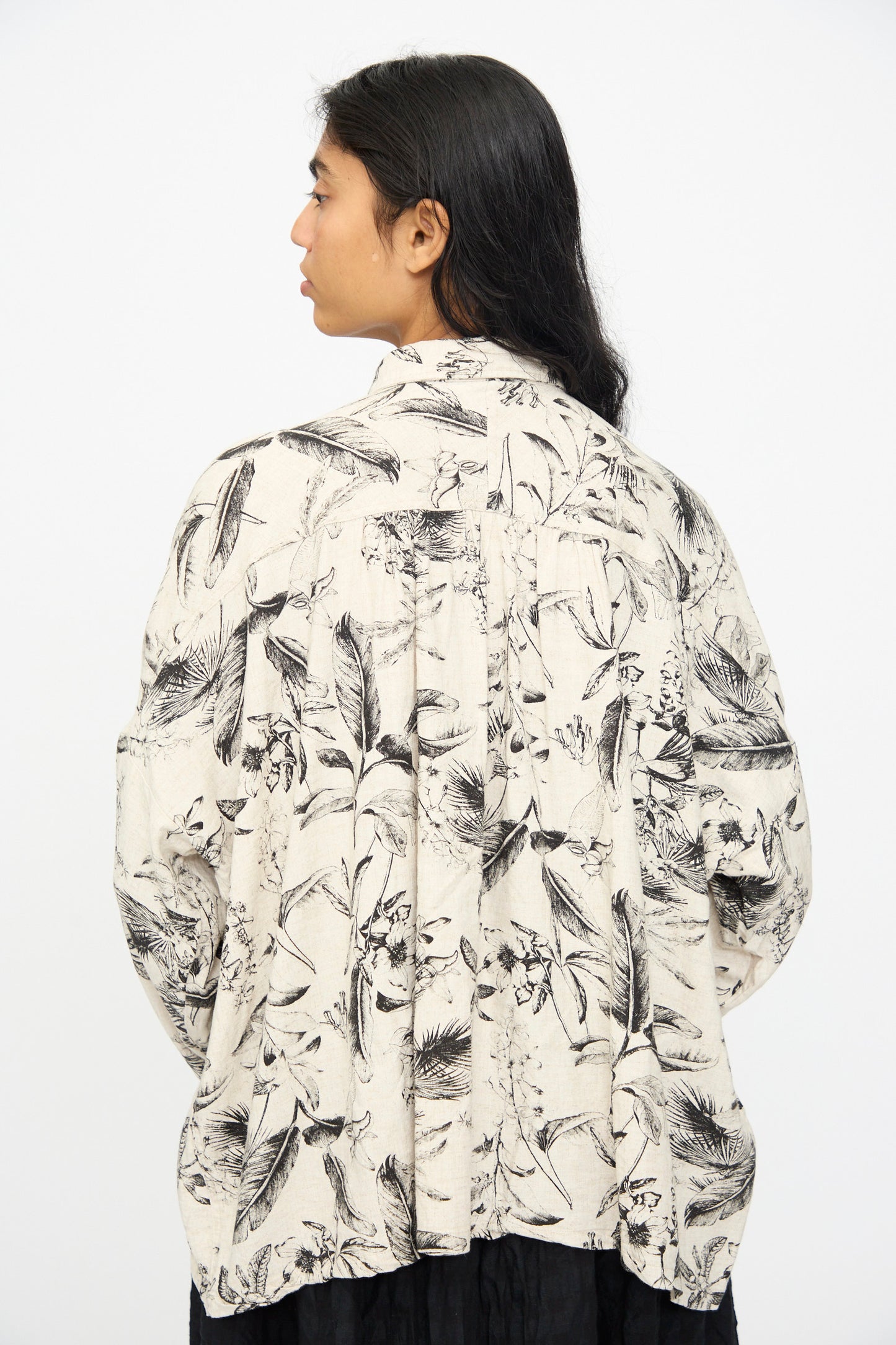 A person with long dark hair is shown from the back, wearing the Ichi Antiquités Botanical Print Shirt in Natural, a relaxed fit shirt featuring a black botanical pattern.