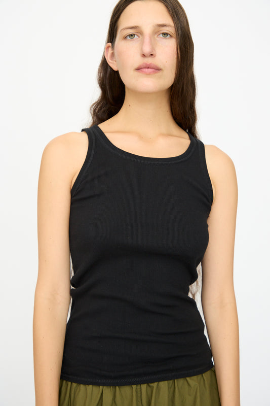 A woman with long brown hair wears the Ichi Antiquités Cotton Cashmere Tank Top in Black, paired with olive green pants, standing against a plain white background.