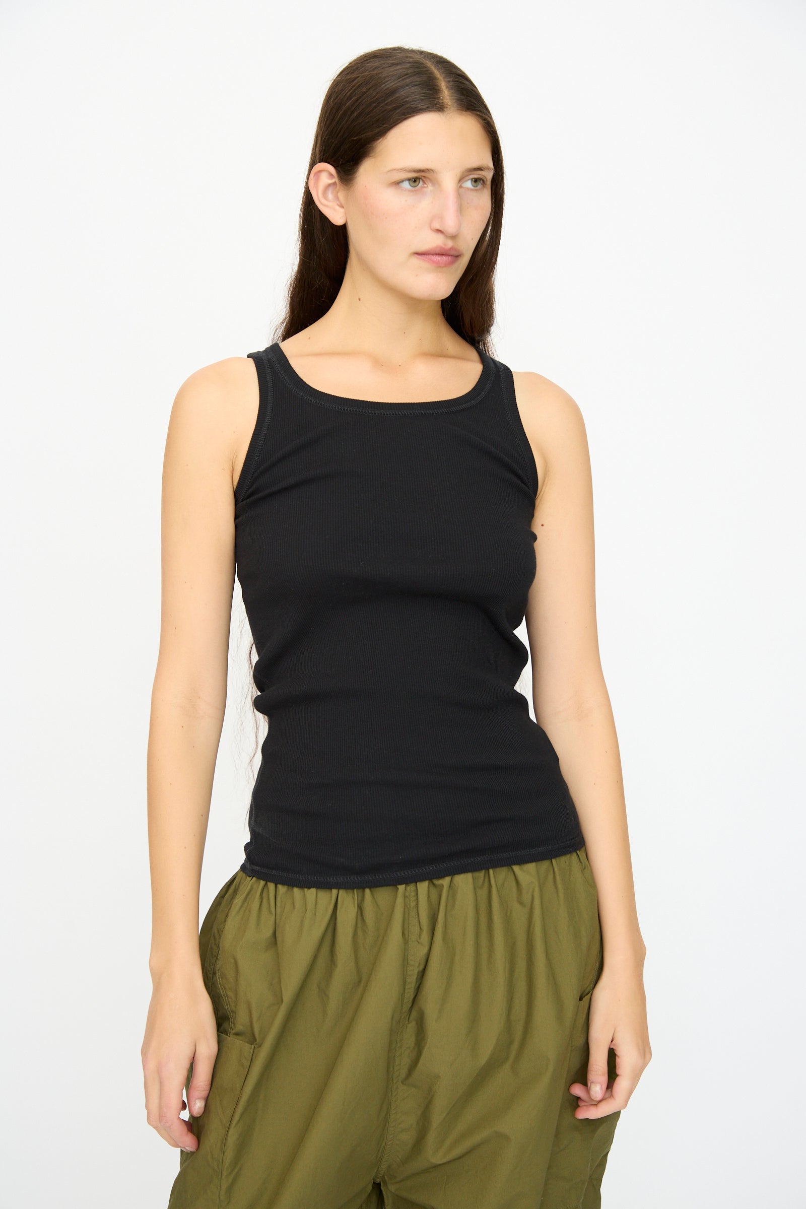 A woman with long brown hair wears the Ichi Antiquités Cotton Cashmere Tank Top in Black and olive green pants, standing against a plain white background.