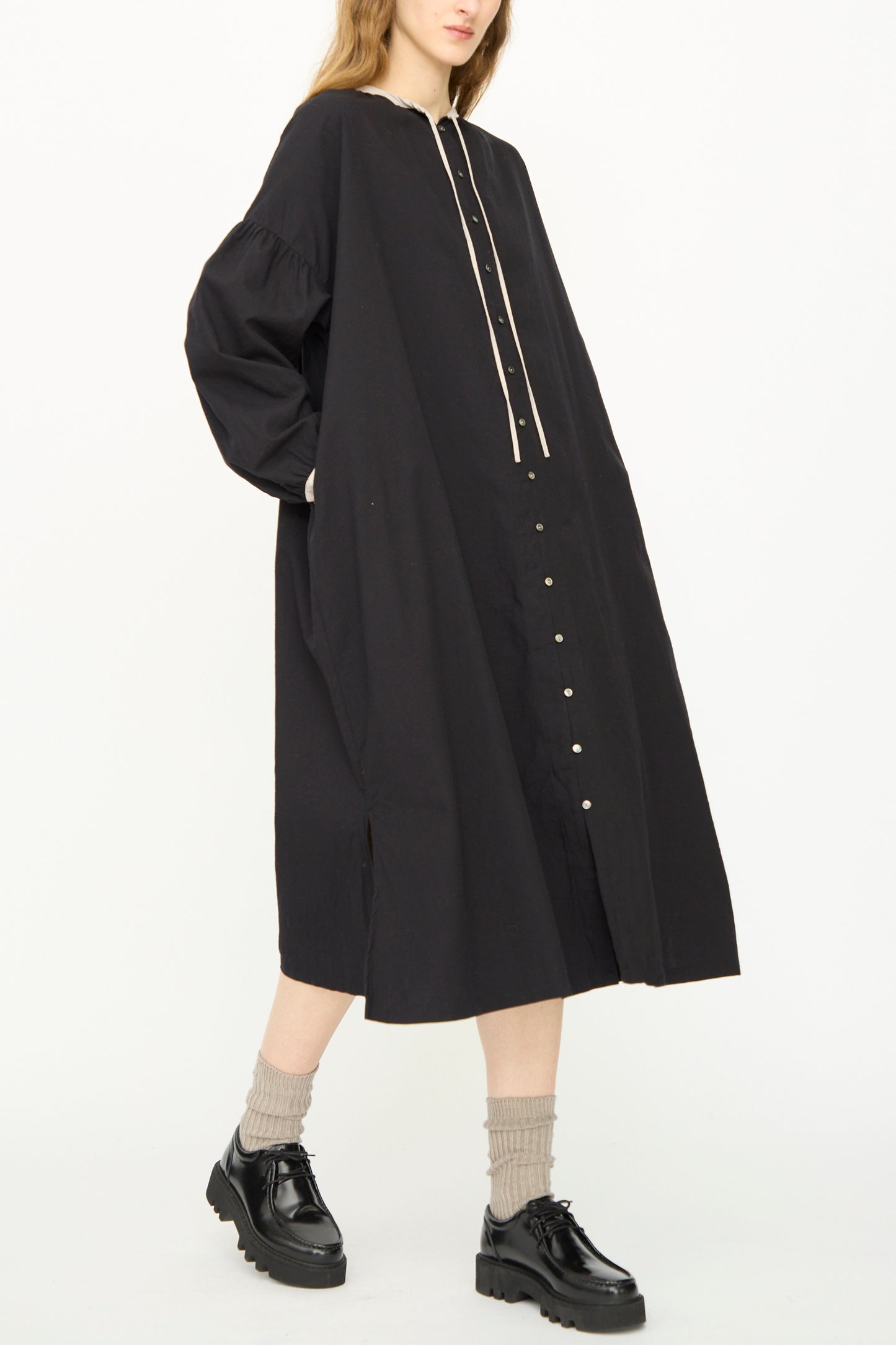 A person wears the Ichi Antiquités Cotton Cashmere Viyella Dress in Black—loose-fitting with long sleeves—paired with chunky black shoes and beige socks, standing against a plain white background.
