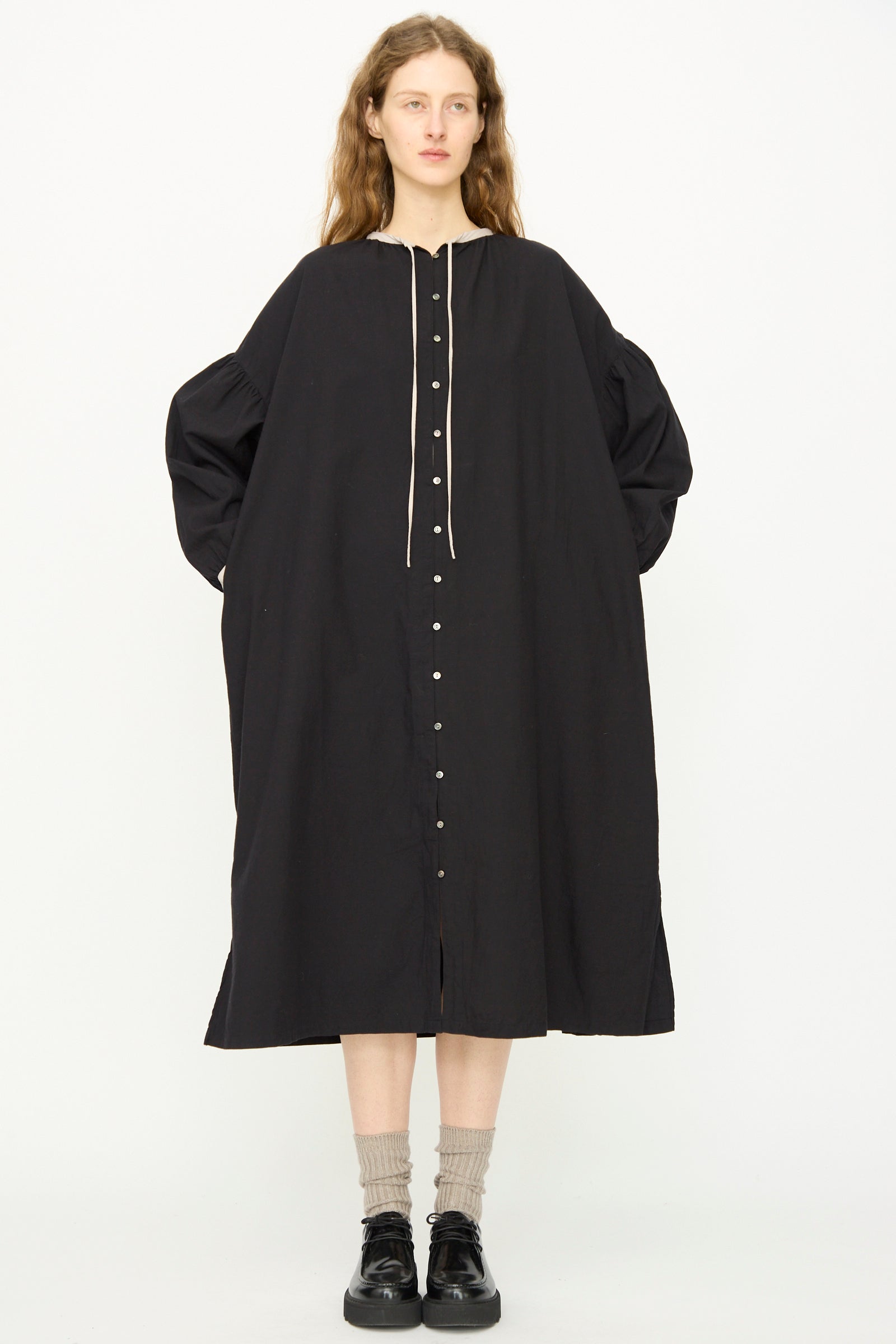 A person stands facing forward in the Ichi Antiquités Cotton Cashmere Viyella Dress in Black, a loose-fitting, button-front midi style made in Japan. Light socks and black shoes complete the timeless look.