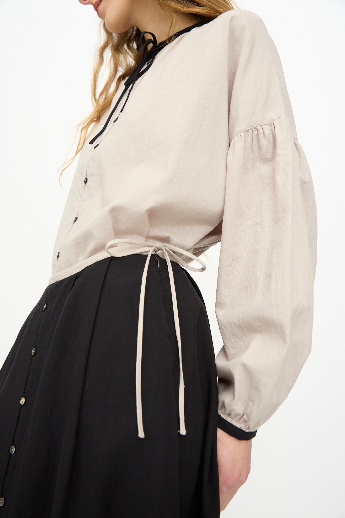 A person wearing a light beige long-sleeve blouse with puffed sleeves and a tied waist, paired with the Cotton Cashmere Viyella Skirt in Black by Ichi Antiquités, made in Japan.