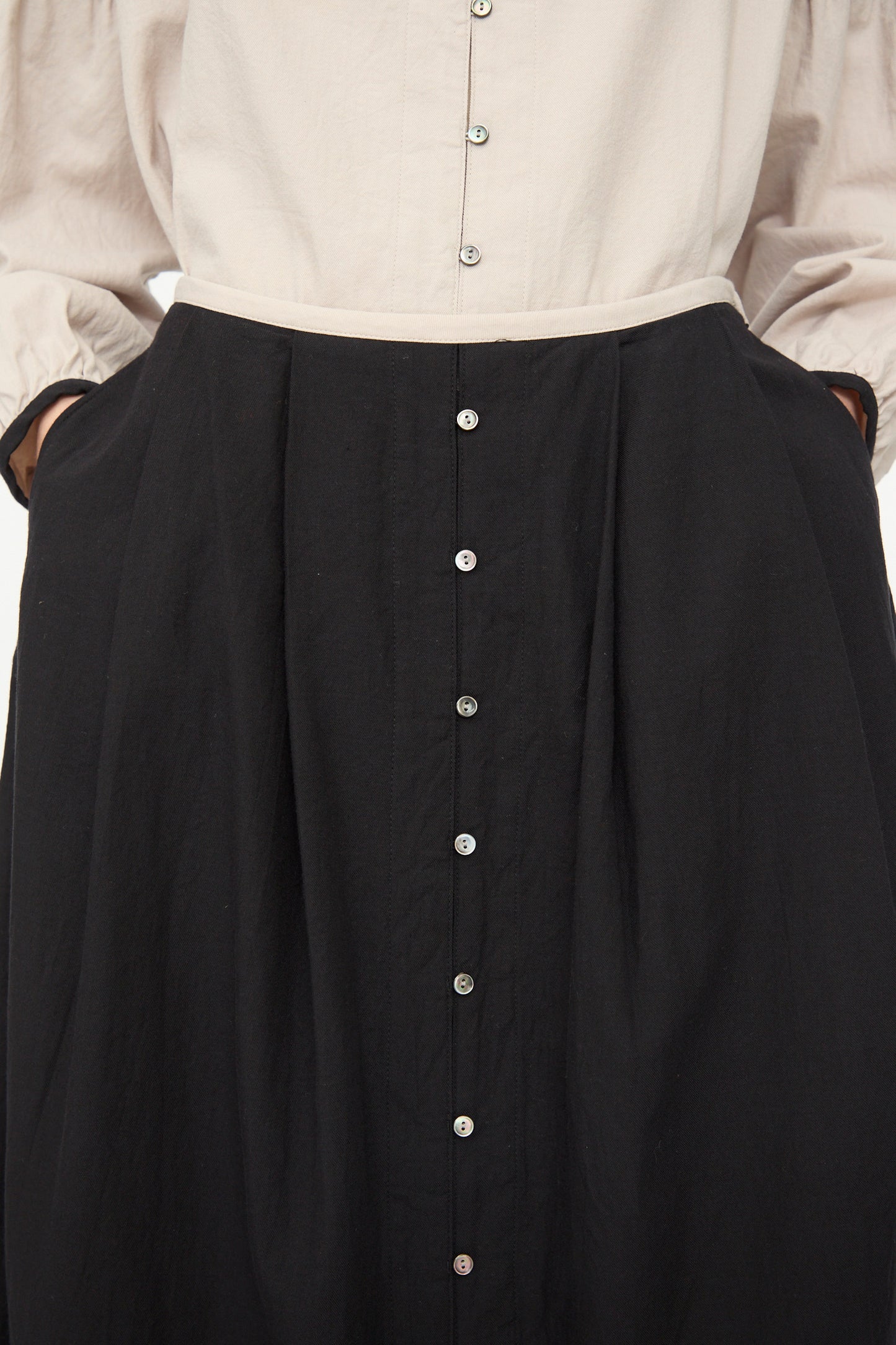 A person wears a light blouse tucked into the Ichi Antiquités Cotton Cashmere Viyella Skirt in Black, a high-waisted A-line with front buttons and pockets, hands resting in the skirt’s pockets.