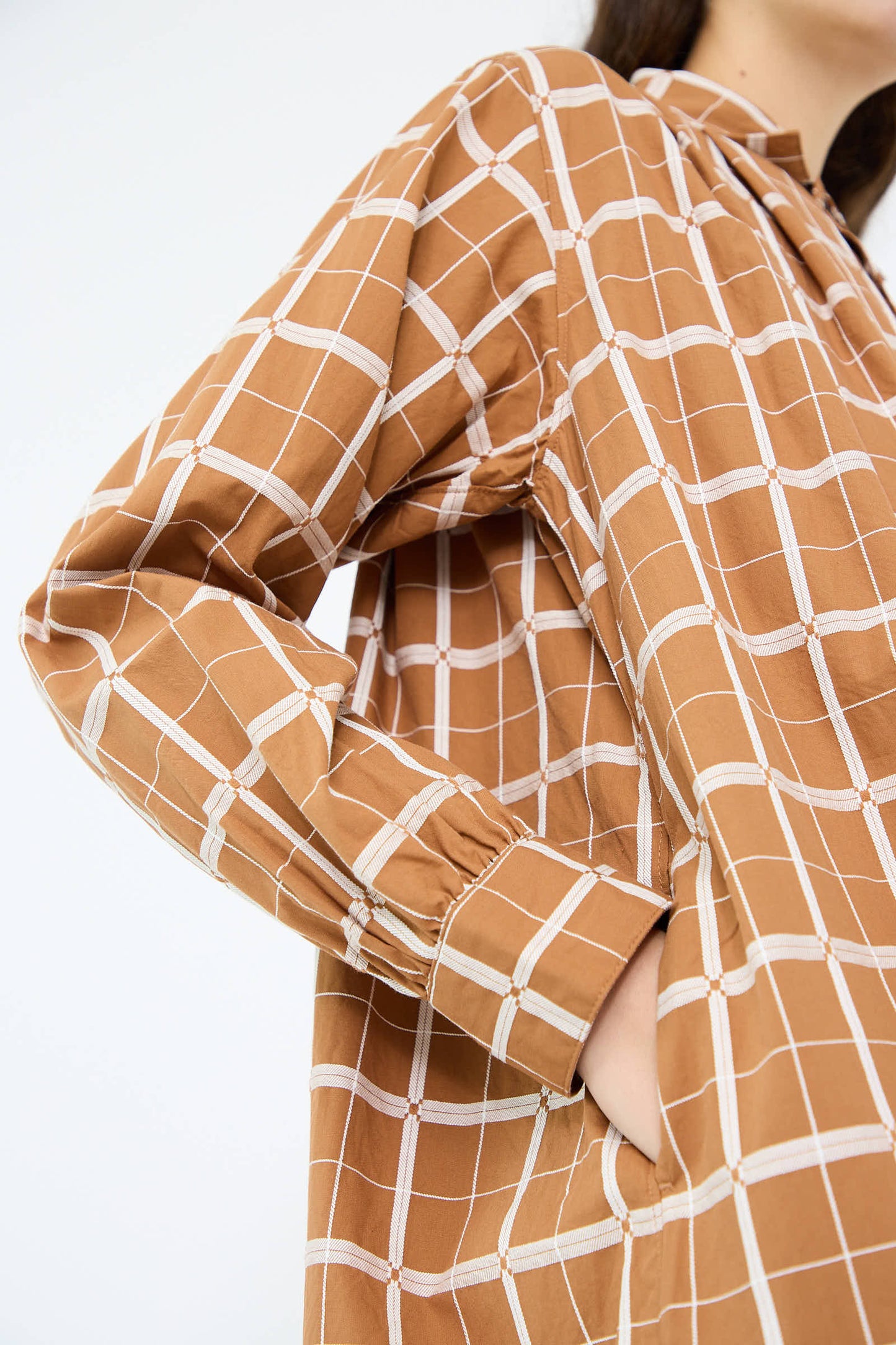 Close-up of a person dressed in the Ichi Antiquités Cotton Dobby Check Dress in brown, featuring white lines, a pocket, and long sleeves.