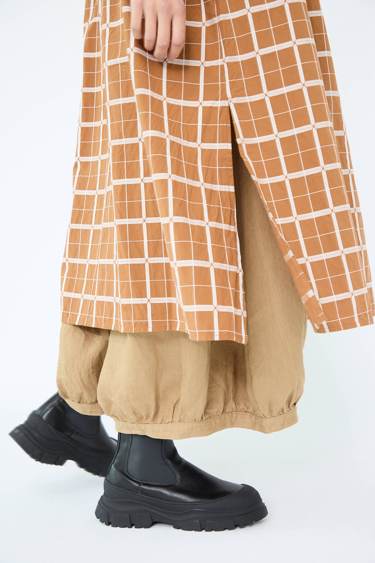 A person wearing black chunky boots, beige pants, and a Cotton Dobby Check Dress in Brown by Ichi Antiquités.